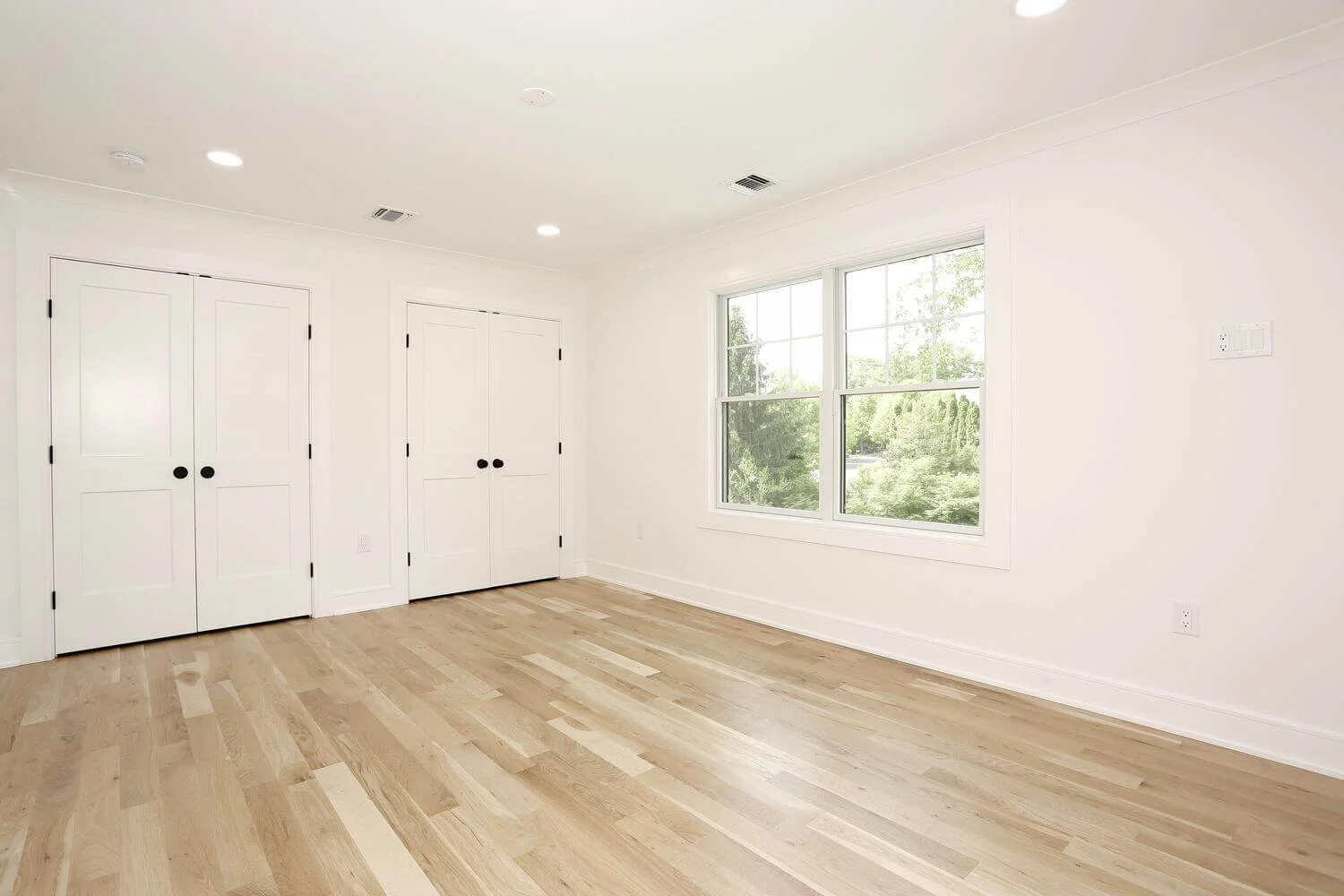 Bedroom with double closet doors, recessed ceiling lights, and light oak floors in a Park Ridge modern farmhouse by Dadak LLC.