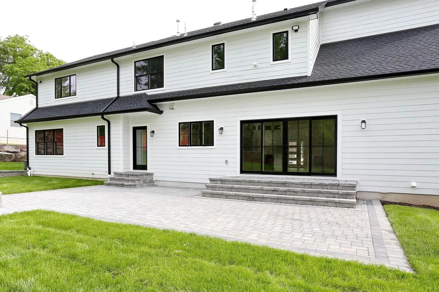 Backyard patio overlooking green lawn and tree-lined property in a Park Ridge modern farmhouse by Dadak LLC.