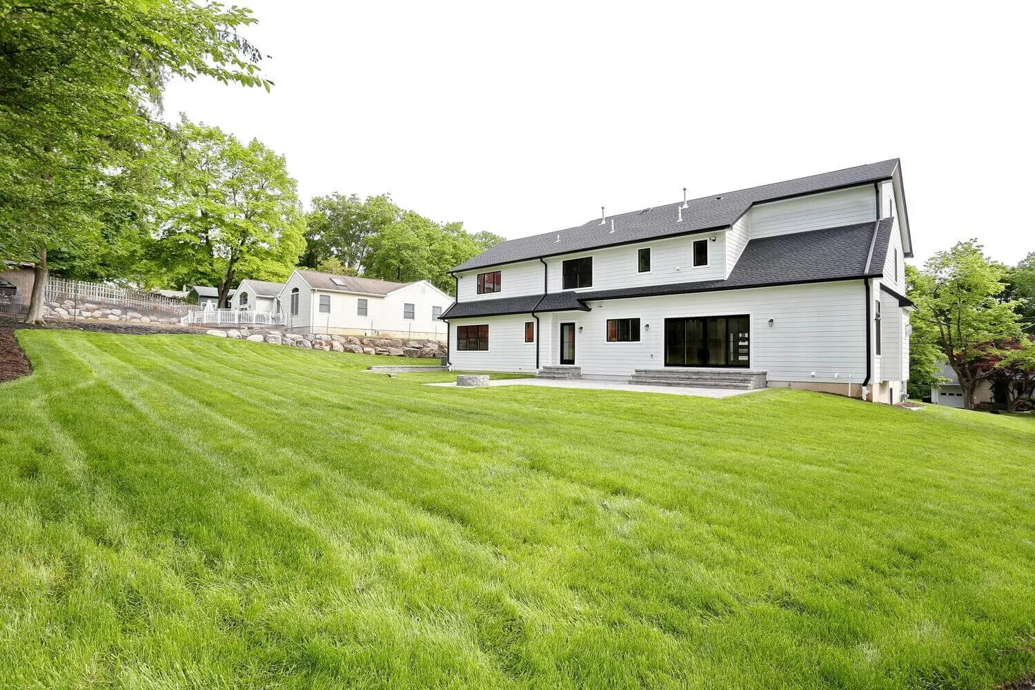 Backyard with open grassy area, mature landscaping, and privacy fencing behind a modern farmhouse in Park Ridge by Dadak LLC.