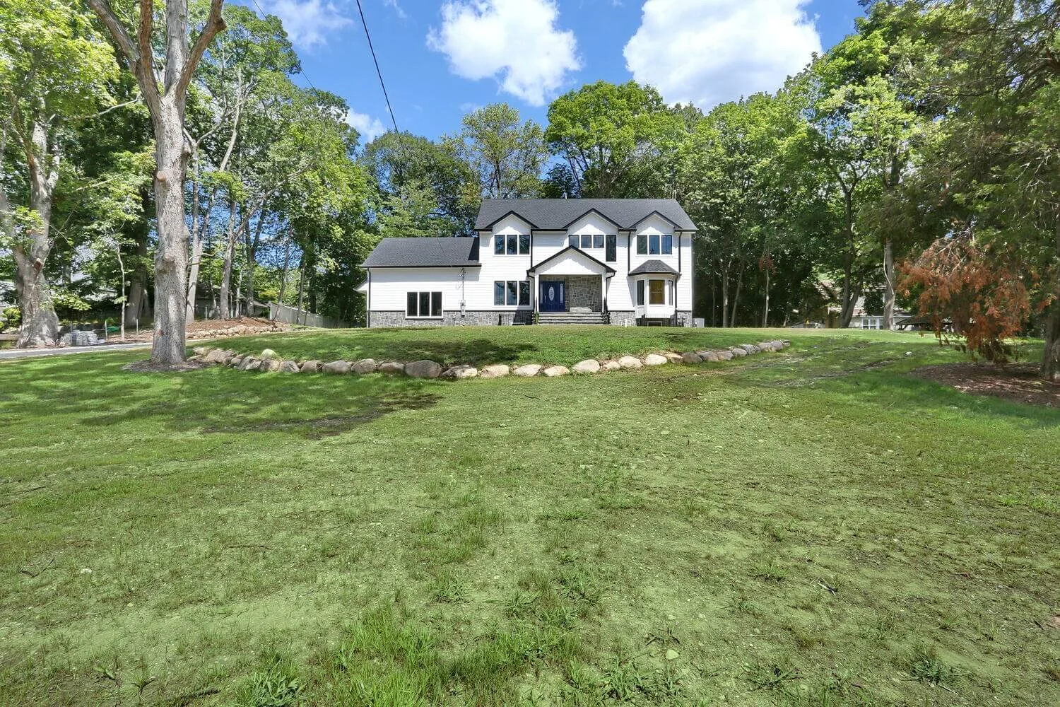 Wide view of Montvale NJ custom home with large front yard, stone border, and mature trees in the background.