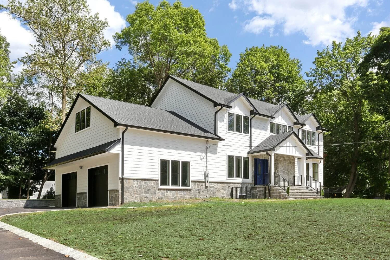 Modern farmhouse in Montvale NJ built by Dadak LLC with white board-and-batten siding, black trim, and front stone porch.