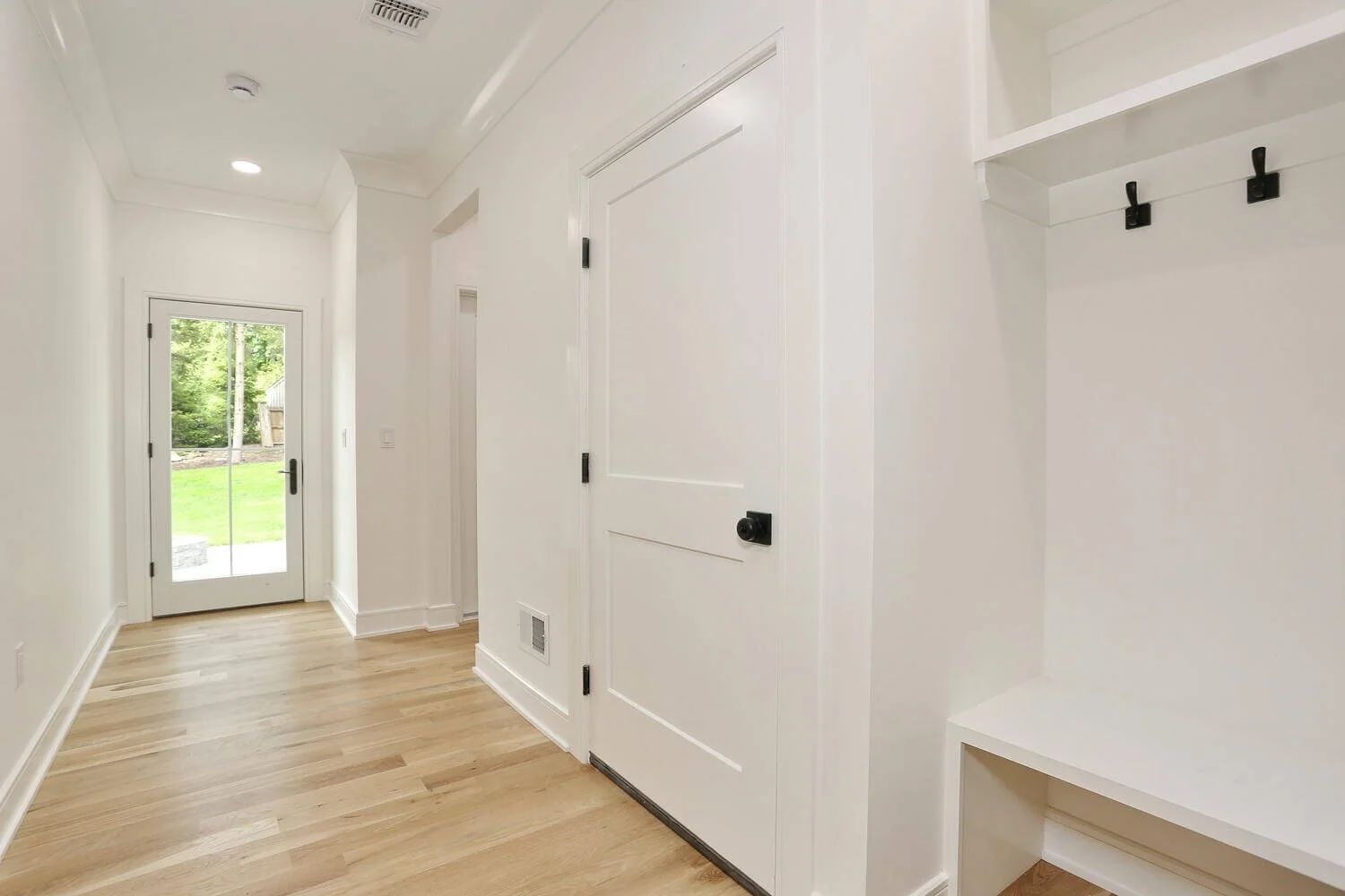 Bright mudroom hallway with white door leading to backyard, showcasing custom millwork and hardwood floors by Dadak LLC in Park Ridge, NJ.