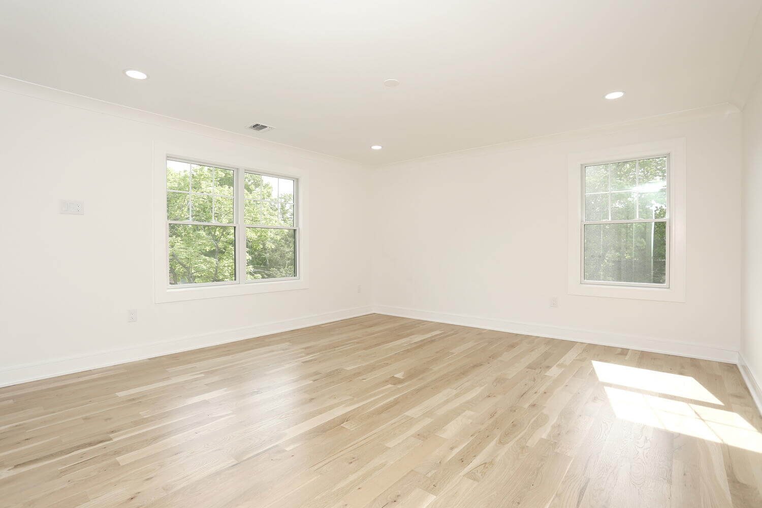 Spacious bedroom with light hardwood flooring, recessed lighting, and large windows overlooking greenery in a Park Ridge modern farmhouse by Dadak LLC.