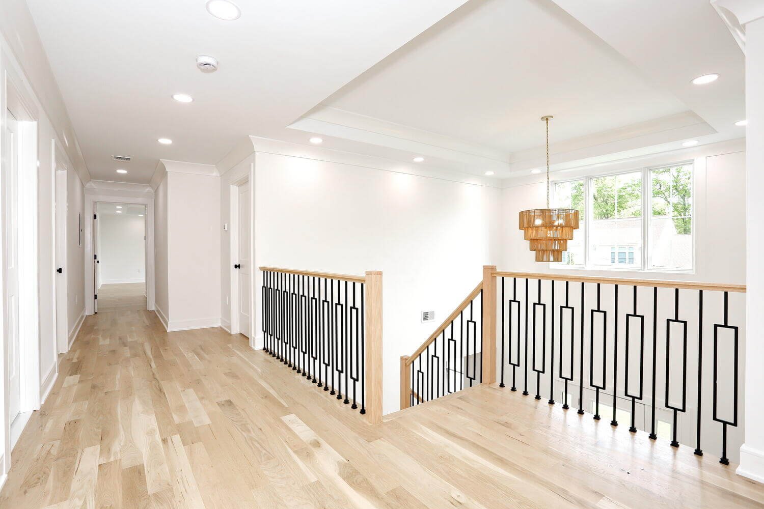 Bright upstairs landing with black metal railing and natural light, connecting bedrooms in a modern farmhouse by Dadak LLC, Park Ridge, NJ.