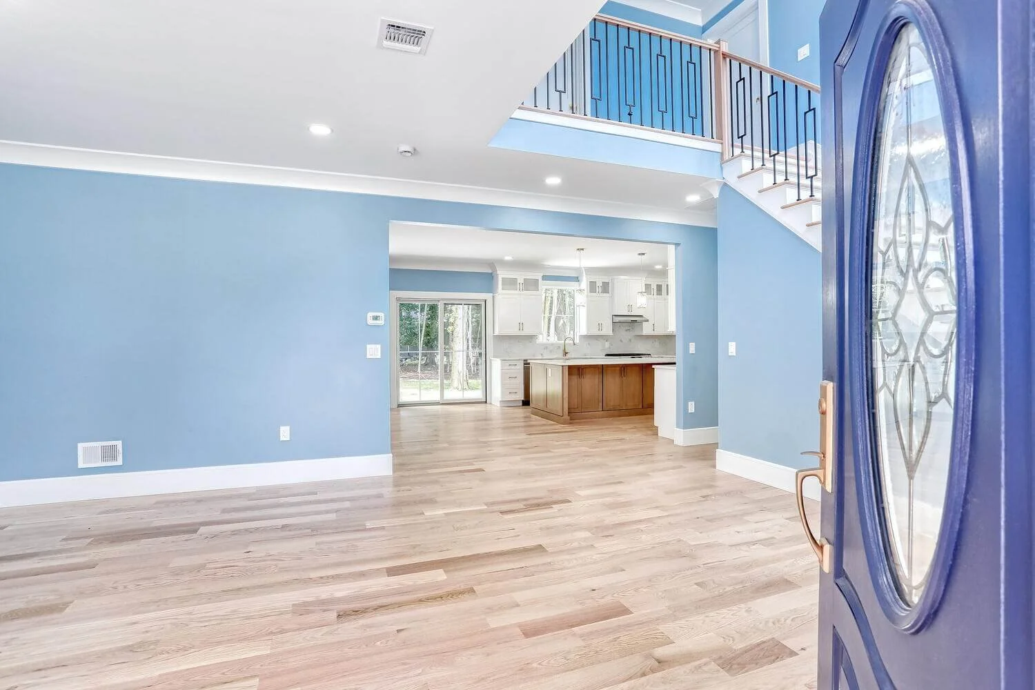 Foyer and open living area of a Montvale custom home by Dadak LLC, featuring blue accent walls, hardwood floors, and views into the kitchen.