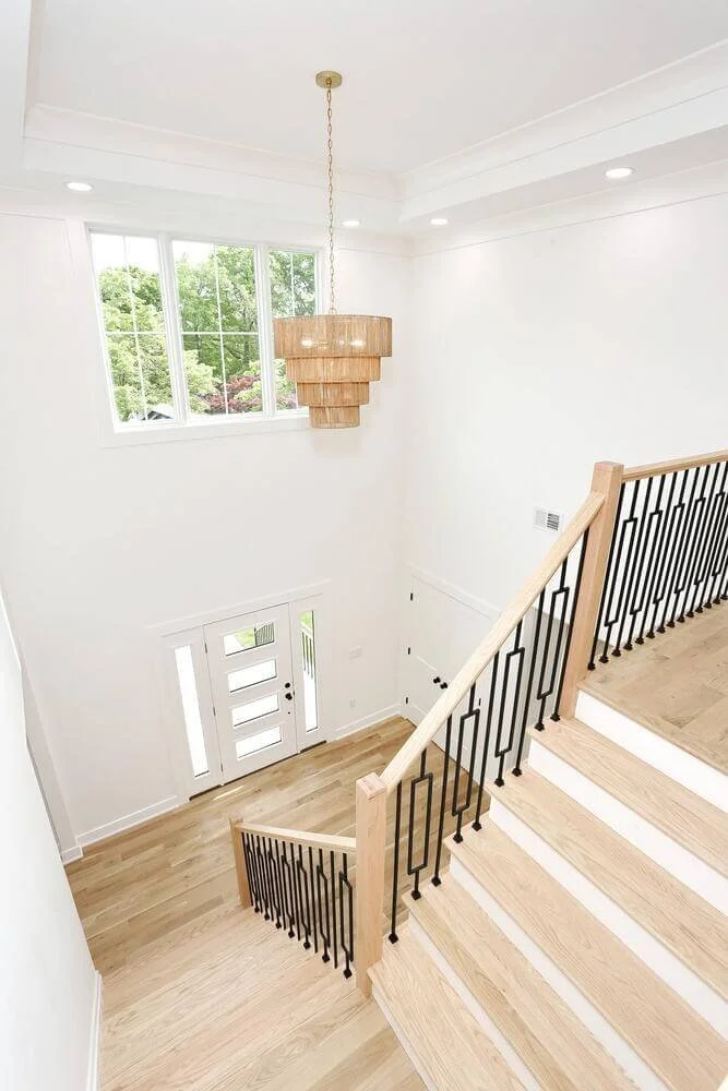Elegant staircase and chandelier view from the upper landing in a two-story foyer of a Park Ridge modern farmhouse built by Dadak LLC.