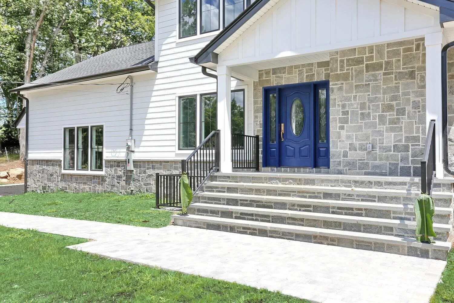 Front entry of a custom home in Montvale NJ featuring blue double doors, gray stone steps, and white siding.