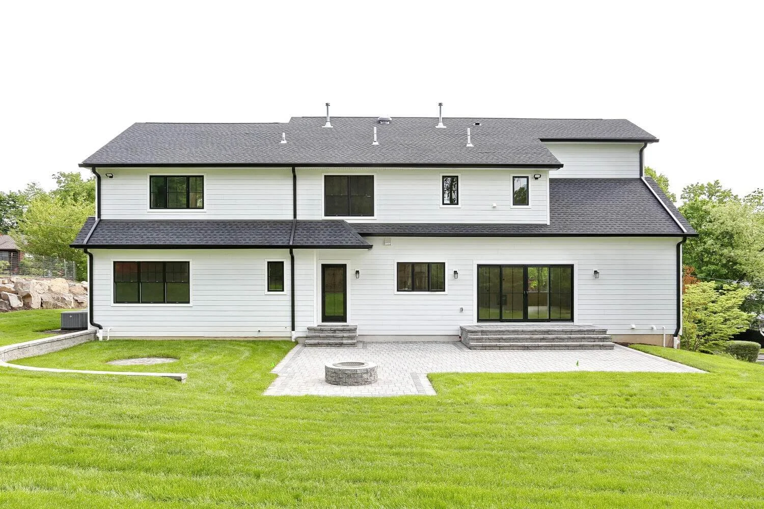 Rear exterior of modern farmhouse featuring white siding, black trim, and large backyard space in Park Ridge by Dadak LLC.