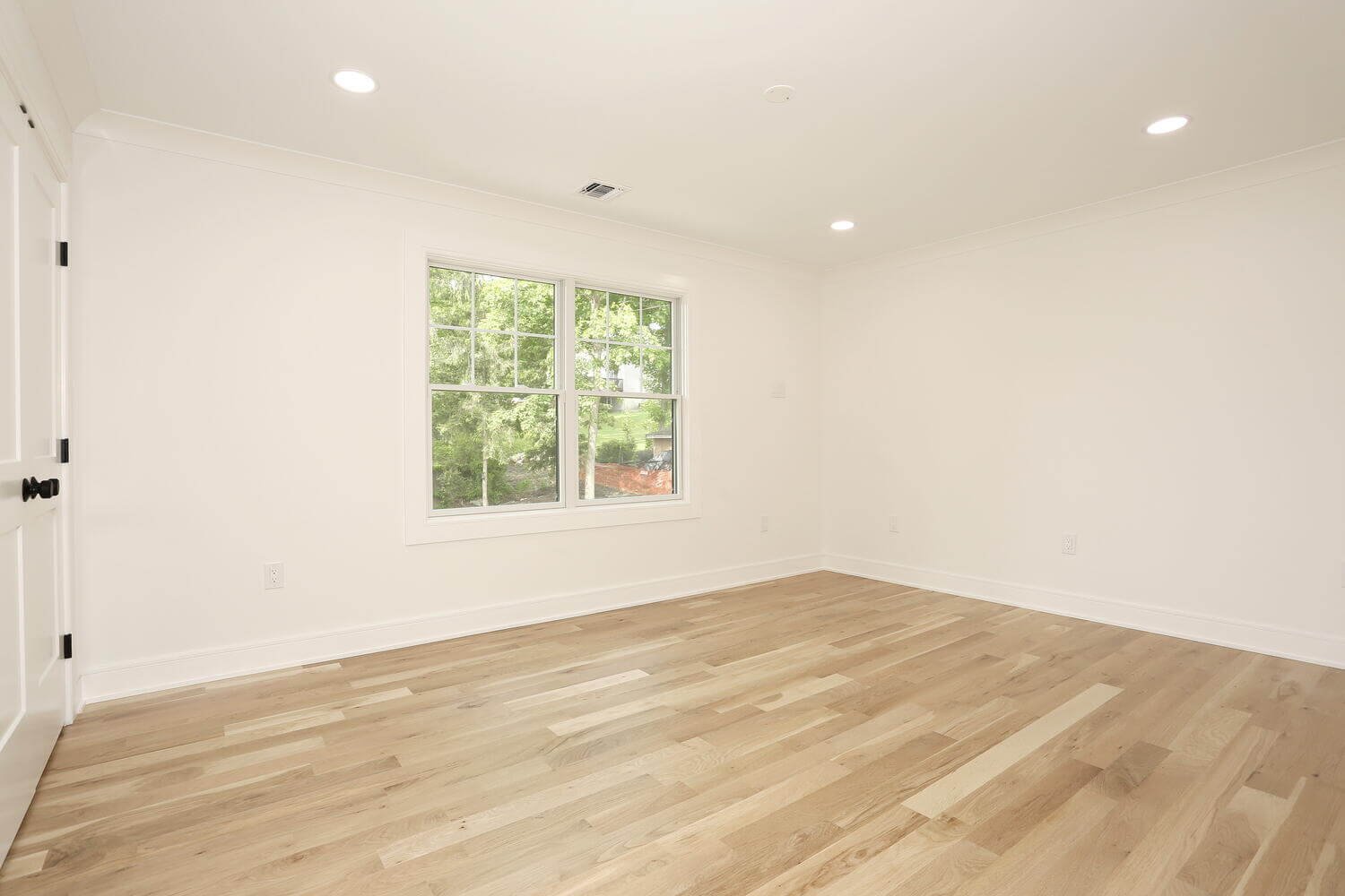 Bright bedroom with large window and hardwood flooring in a Park Ridge modern farmhouse by Dadak LLC.