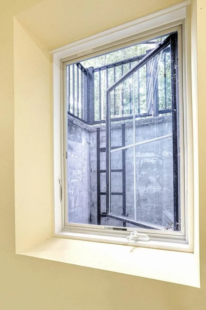 Basement egress window with metal safety ladder and exterior well in Montvale home.