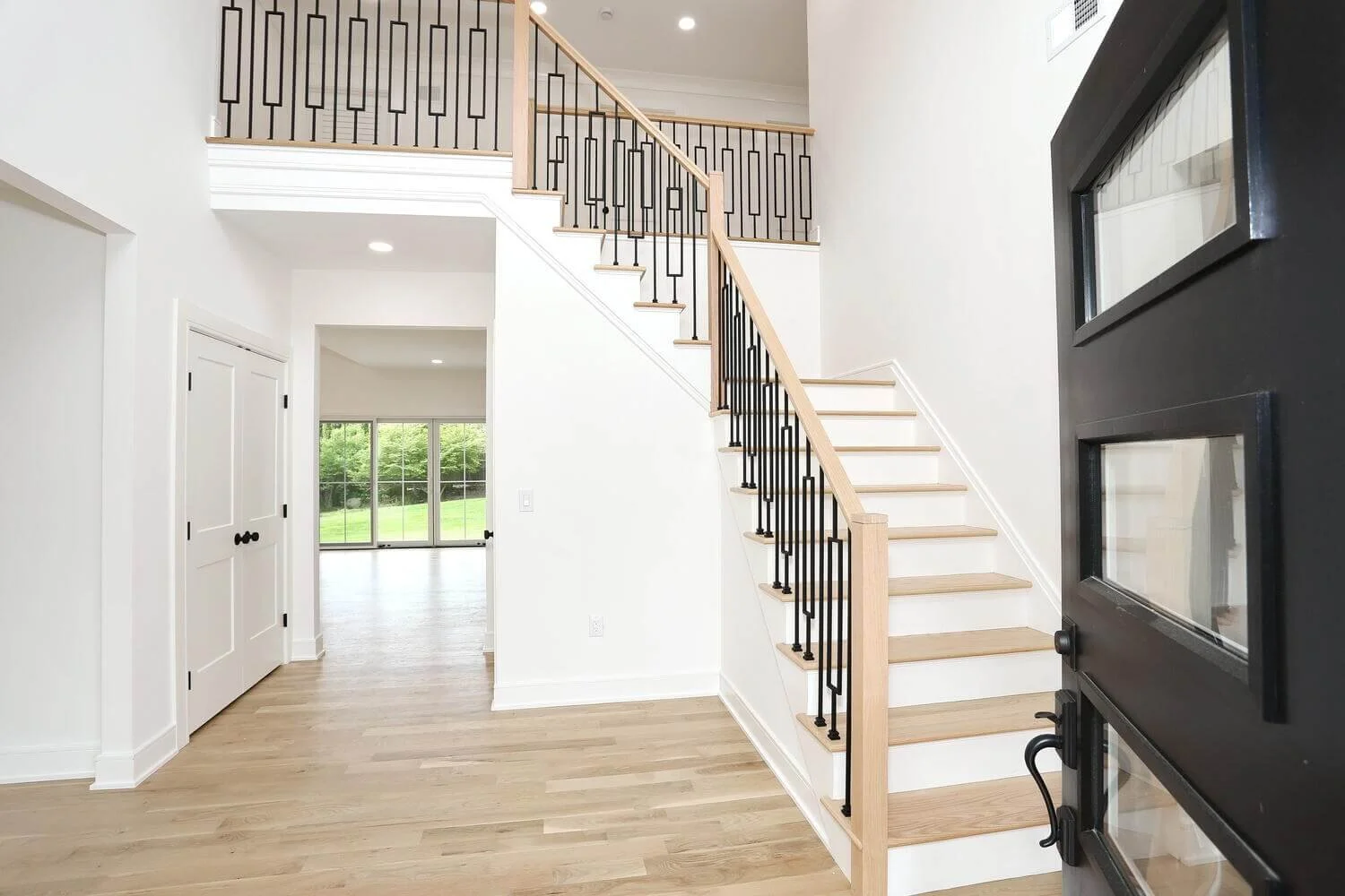 Spacious foyer with modern black railing staircase and light oak floors in a custom home by Dadak LLC in Park Ridge, NJ.