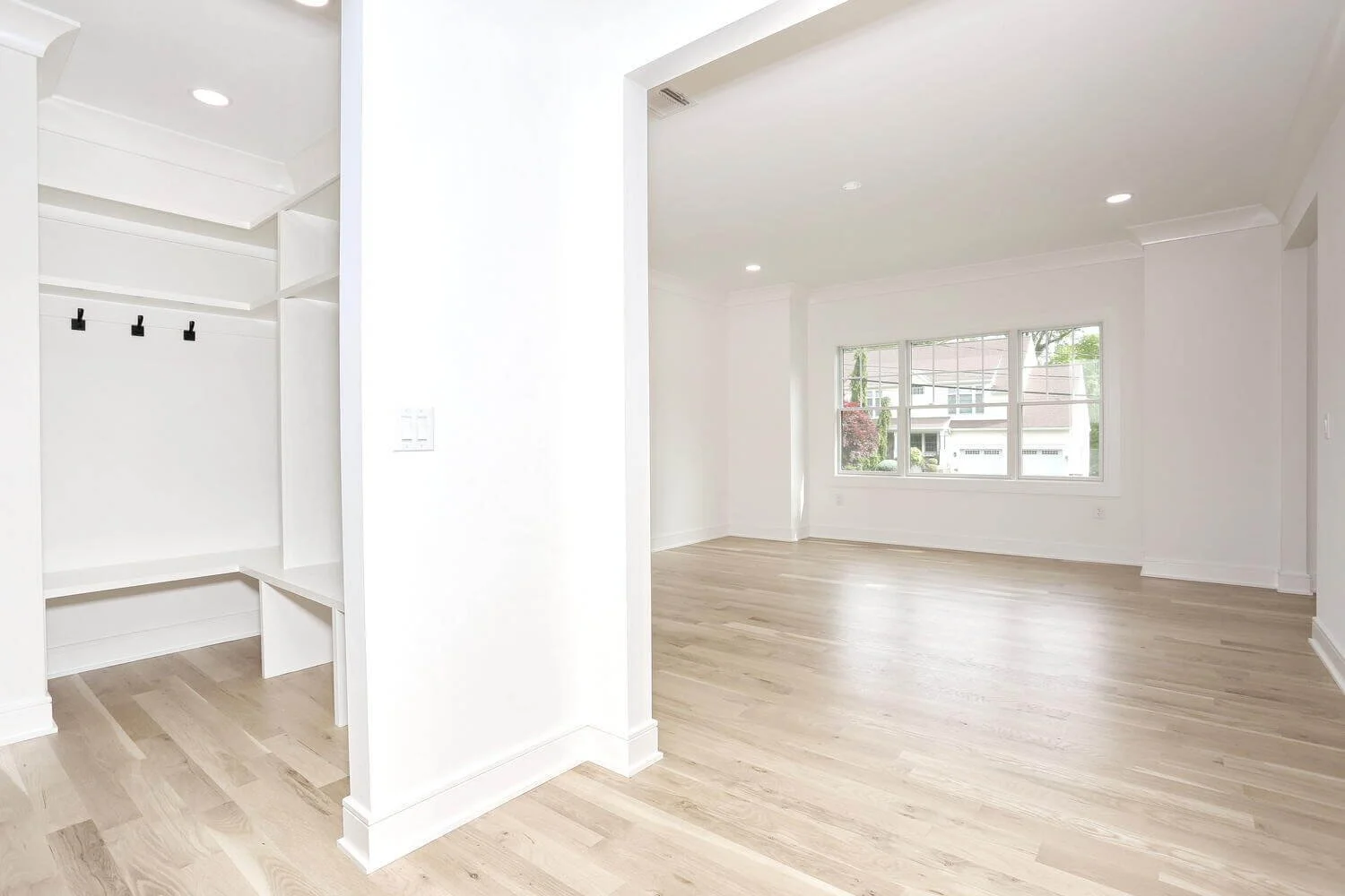 Spacious living room with view toward staircase and kitchen area, featuring light oak floors in a custom home by Dadak LLC, Park Ridge, NJ.