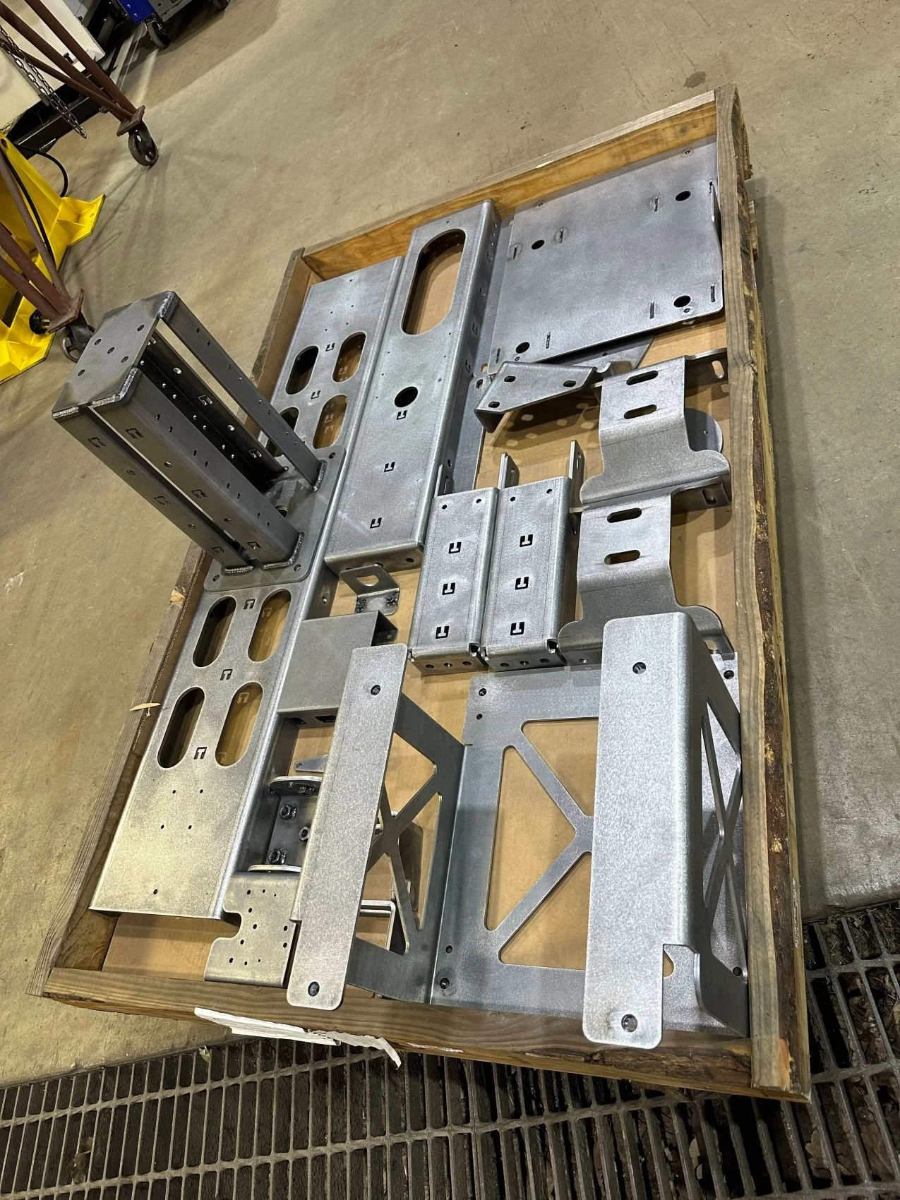 Metal parts and structures arranged on a wooden surface, likely components of a machine or equipment, in an industrial or workshop setting.