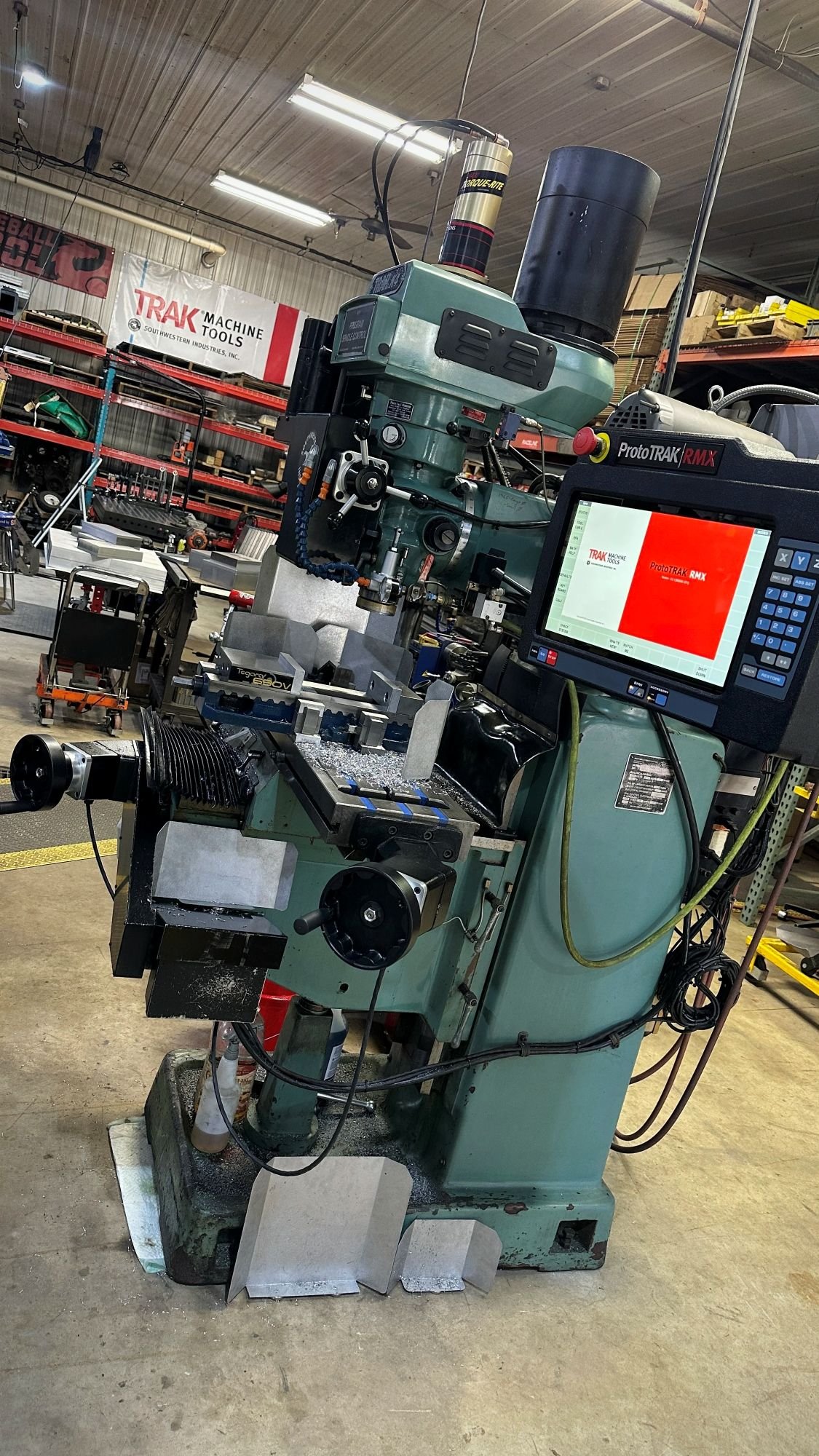 Industrial CNC milling machine in a workshop, with a computer screen displaying the logo 'TRAK MACHINERY TOOLS'.