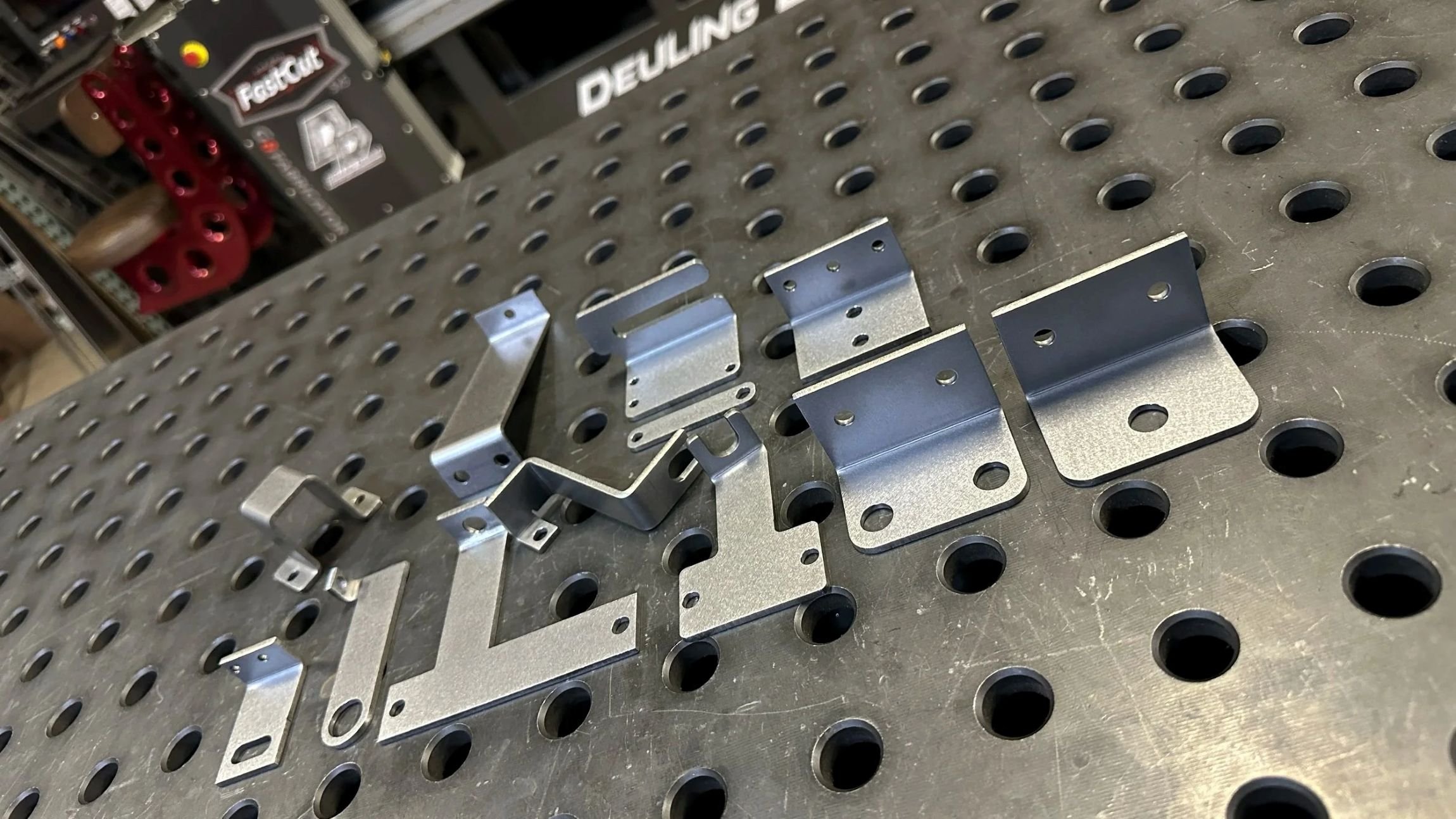 Metal brackets and parts placed on a perforated work table in a workshop or manufacturing setting.