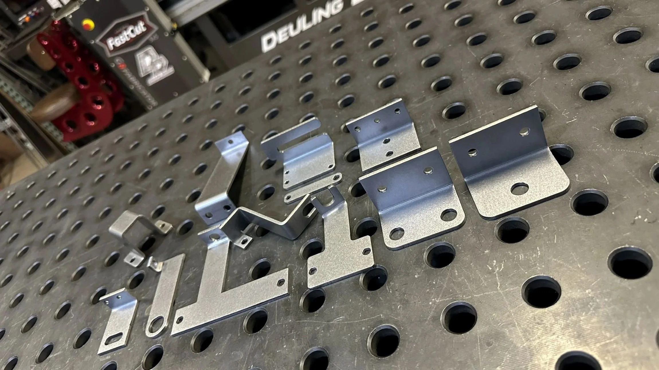 Metal brackets and parts placed on a perforated work table in a workshop.