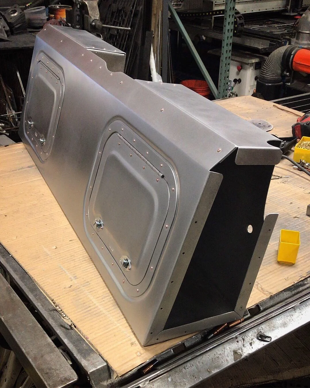Custom fabricated metal box with access doors on a workbench in a workshop.