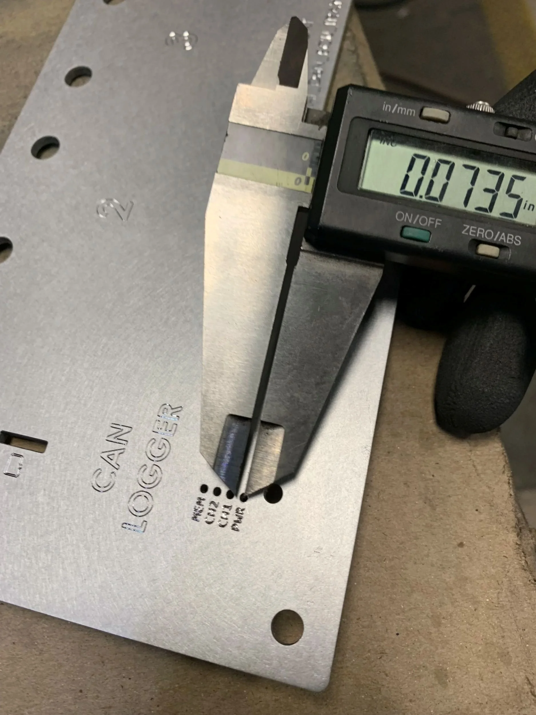 Close-up of a digital caliper measuring the thickness of a metal plate, showing a reading of 0.0735 inches.