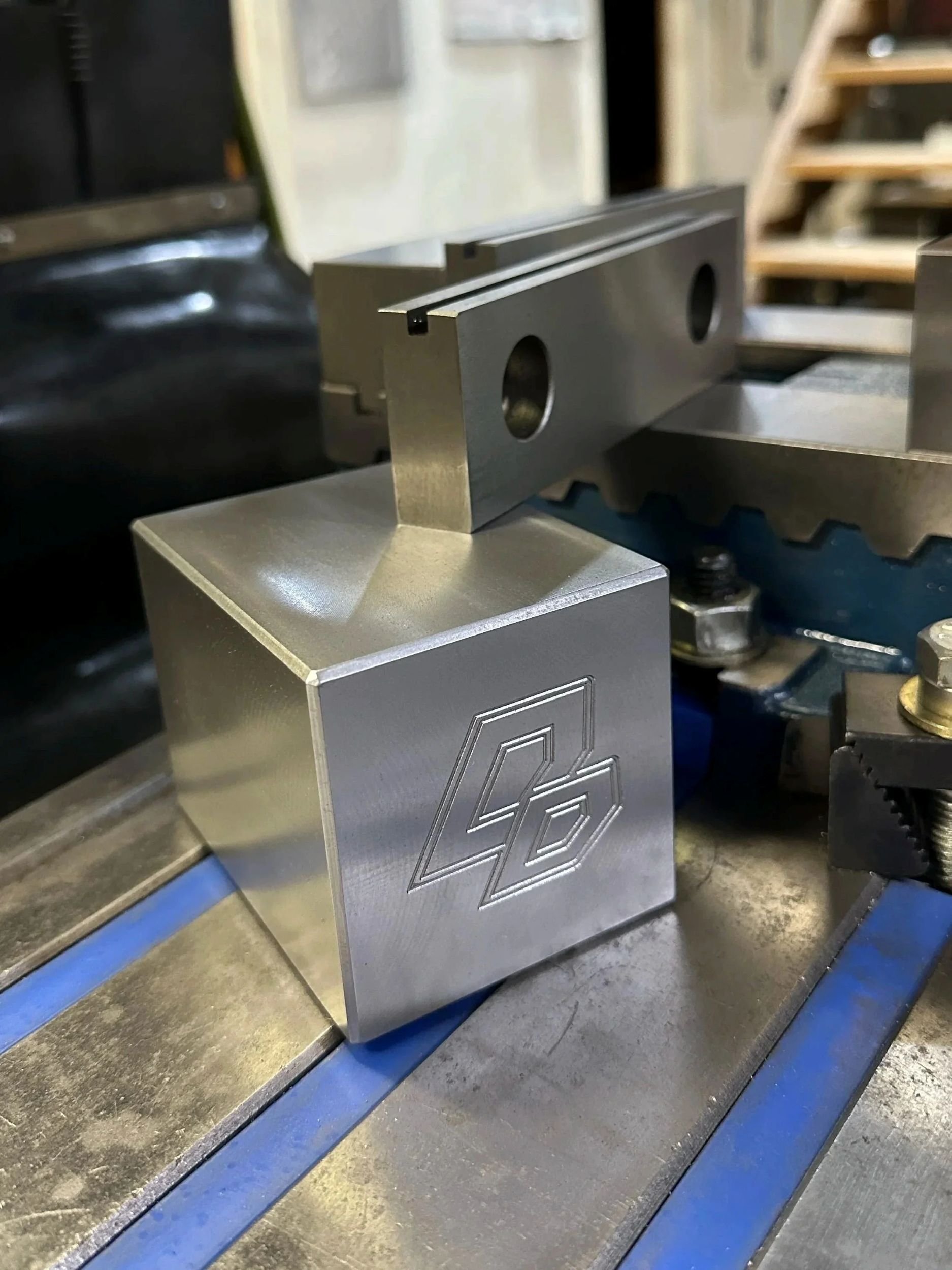 Close-up of a metal block with engraved geometric DD design, placed on a workbench in a workshop.