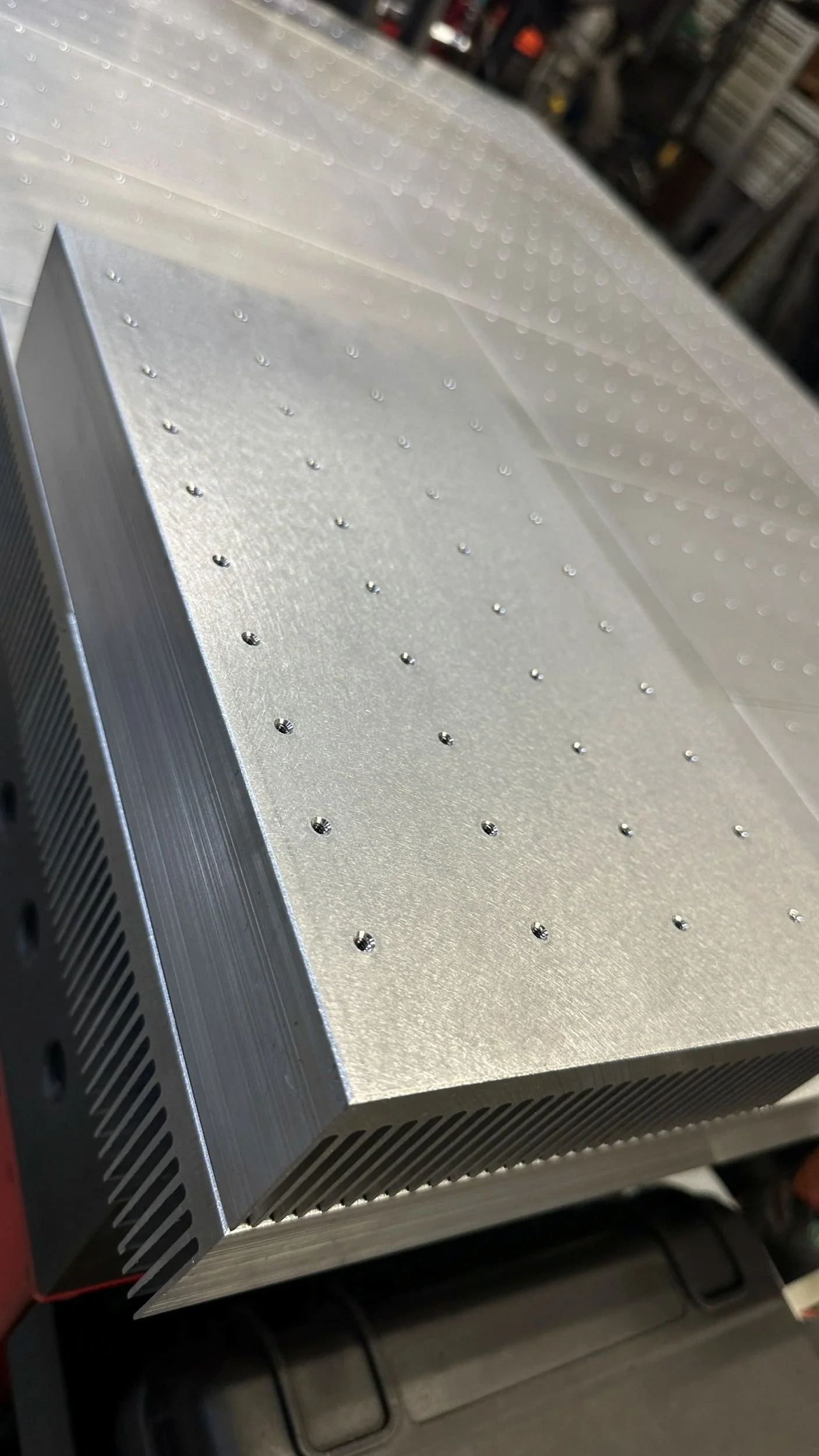 A metal component with a rectangular shape, featuring multiple small evenly spaced holes on its surface, and vent holes on the sides.