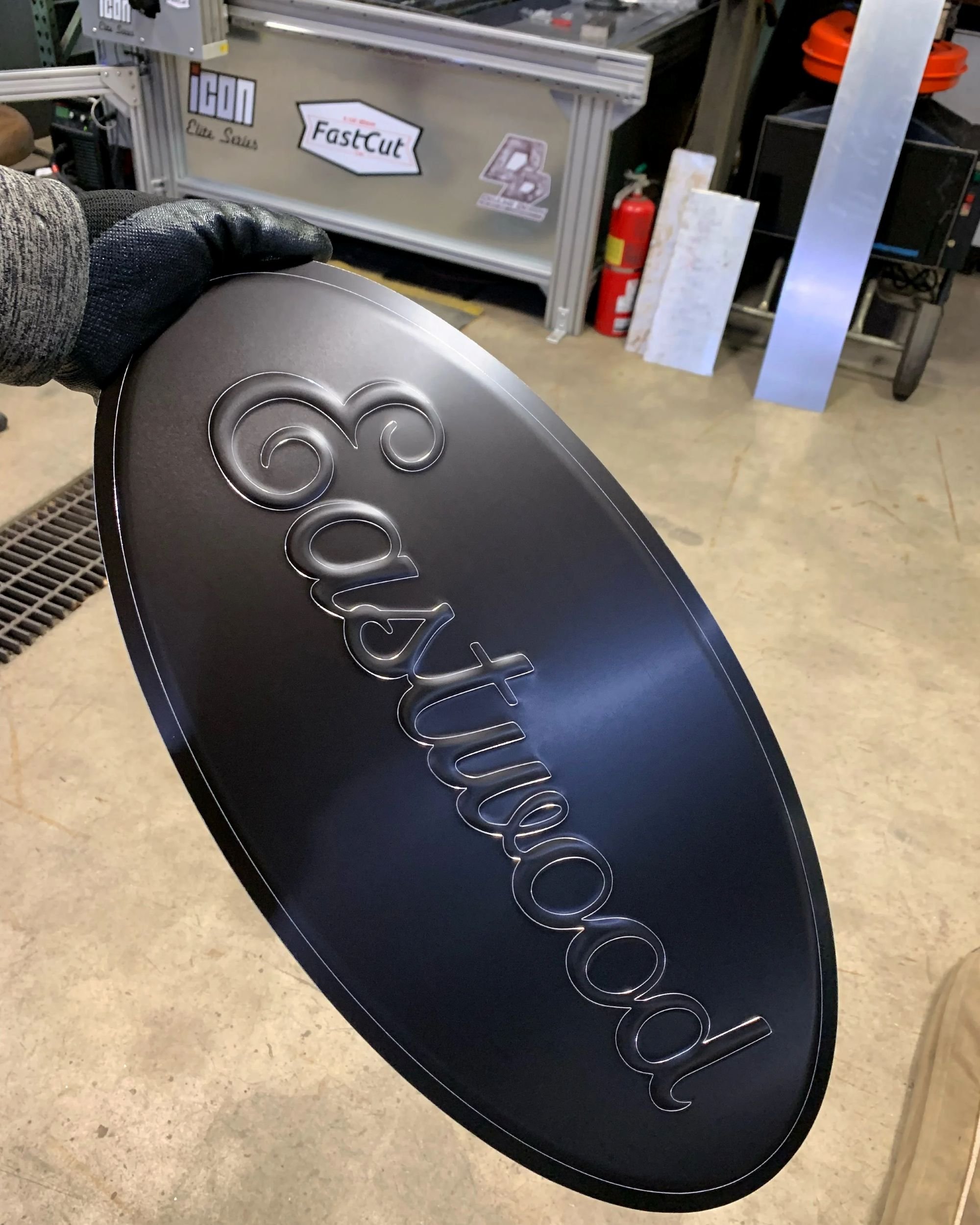 A black metal sign with the word 'Eastwood' in stylized text, being held in hand in a workshop.