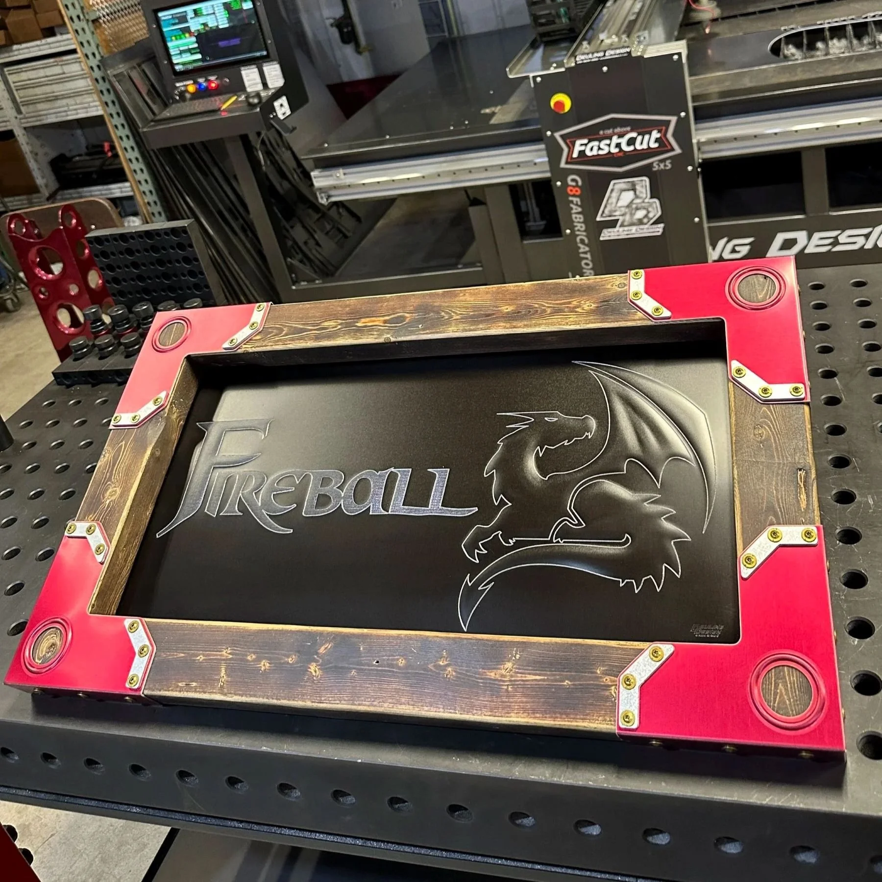 A black bead rolled metal piece with a dragon logo and the word "FIREBALL" on it, placed in a wood frame with red corners.