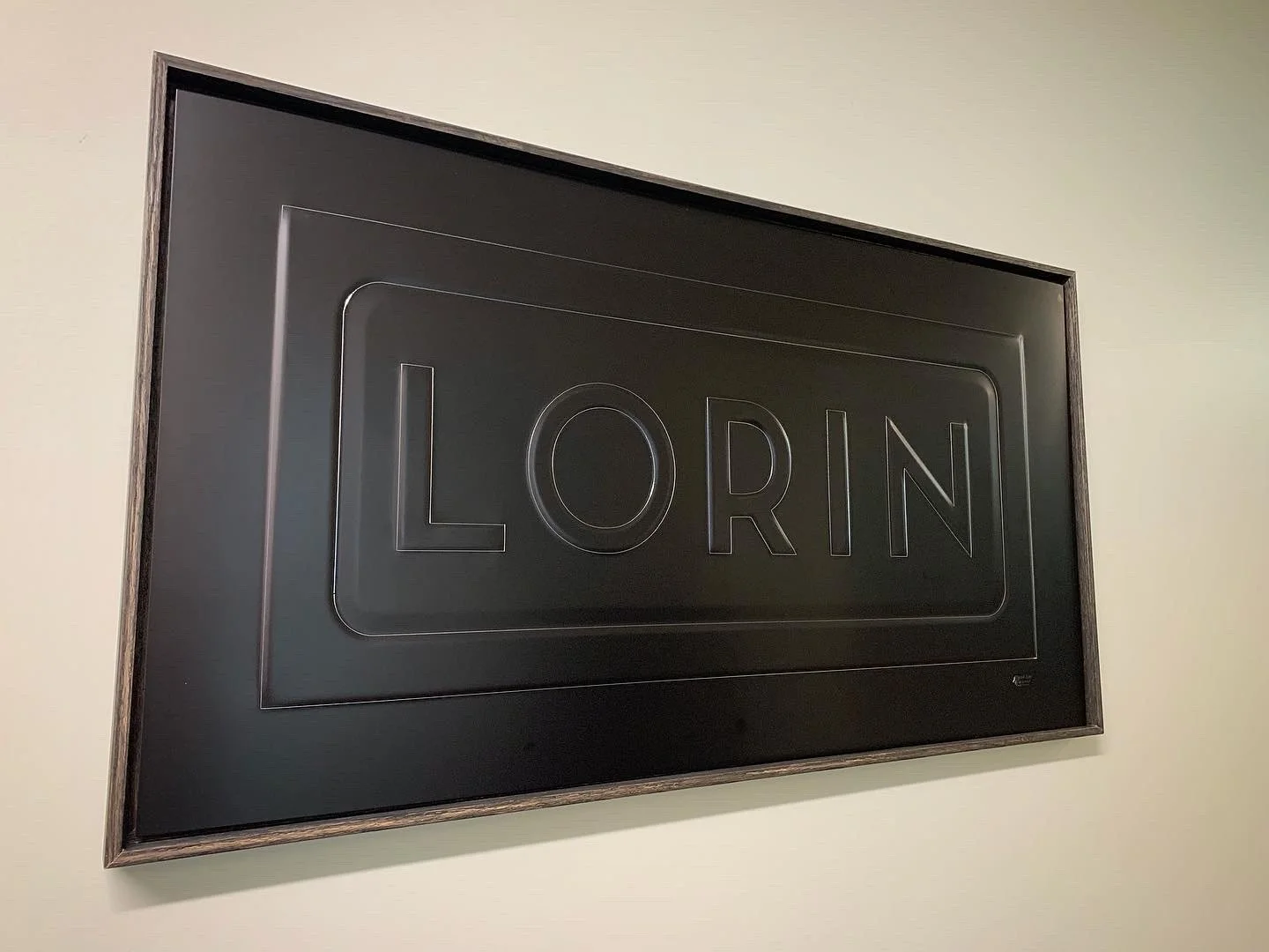 Black metal sign with the word 'LORIN' embossed in large letters, framed in dark wood.