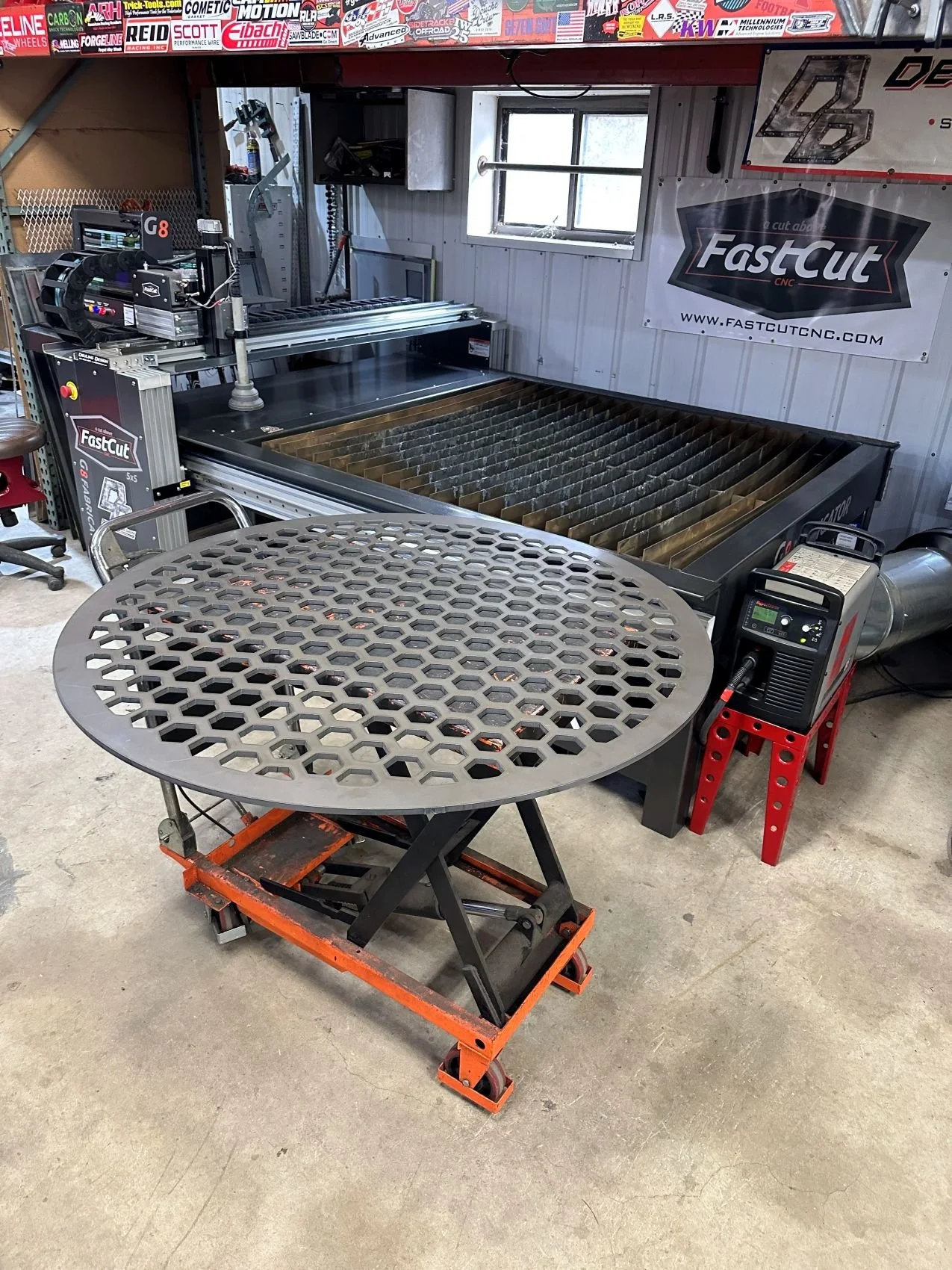 A CNC laser cutting machine in a workshop with a holed, round steel component in front.