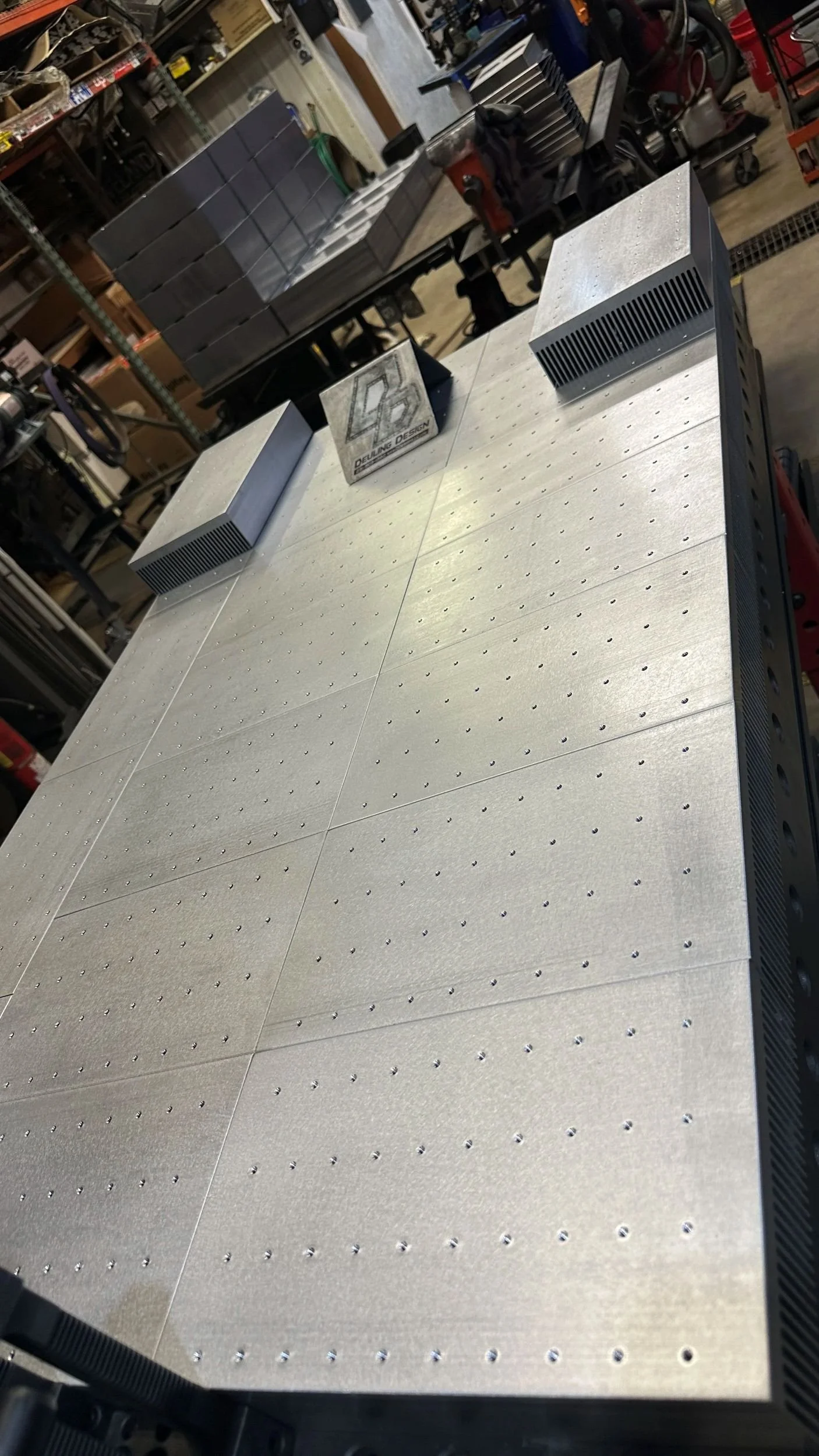Close-up of a metal worktable with a brushed finish, featuring a grid pattern of small holes, possibly used for assembly or fabrication in a workshop.