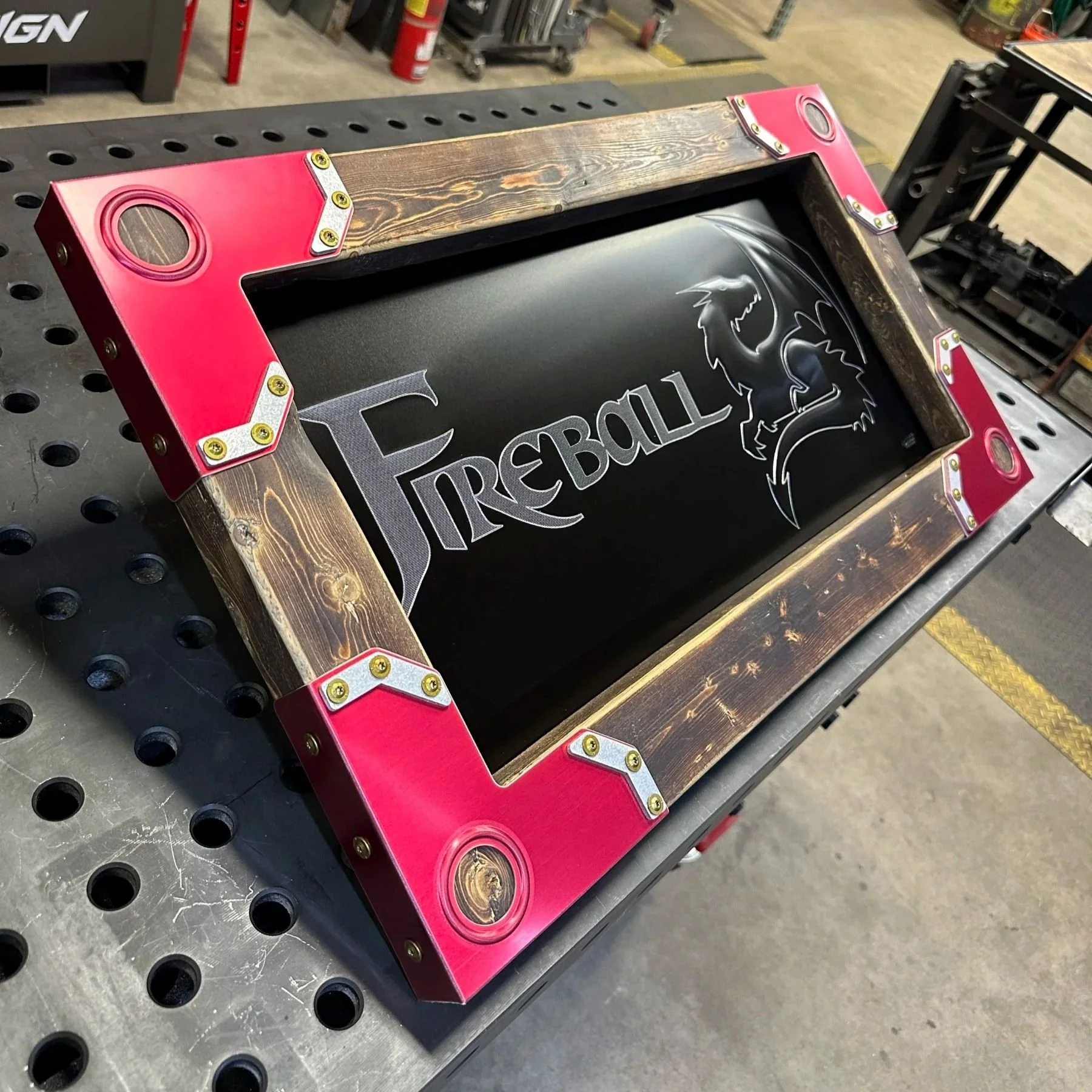 A black bead rolled metal piece with the word "FIREBALL" and a dragon design on it for Fireball Tool, set in a wood frame with red corners.
