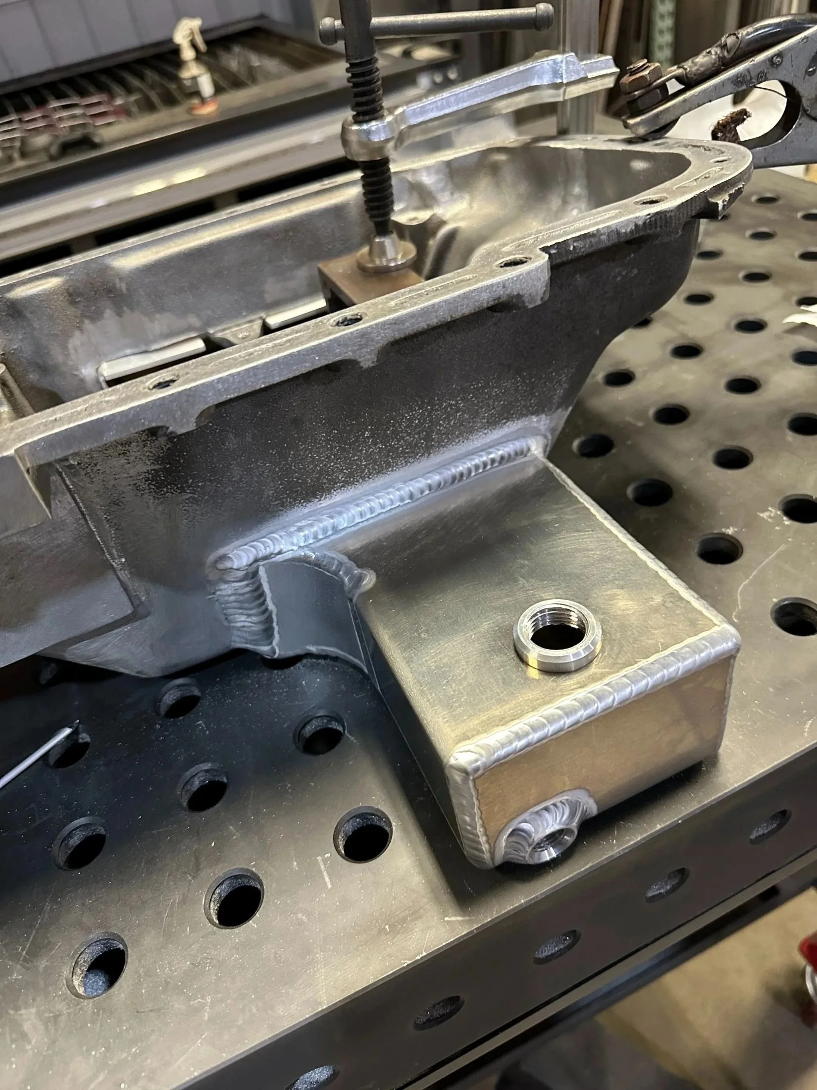 Close-up of metal engine or machinery part being assembled or repaired, with a screw, bolt, and other metal components on a workbench.