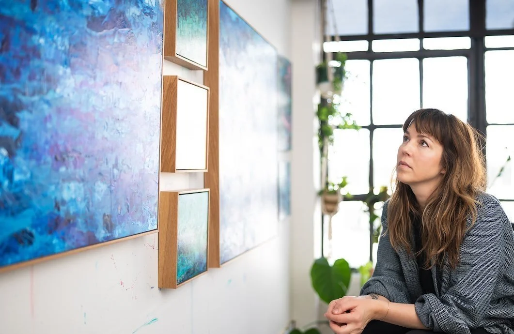 brown haired white female artist Jodi Kendall in her art studio looking at paintings