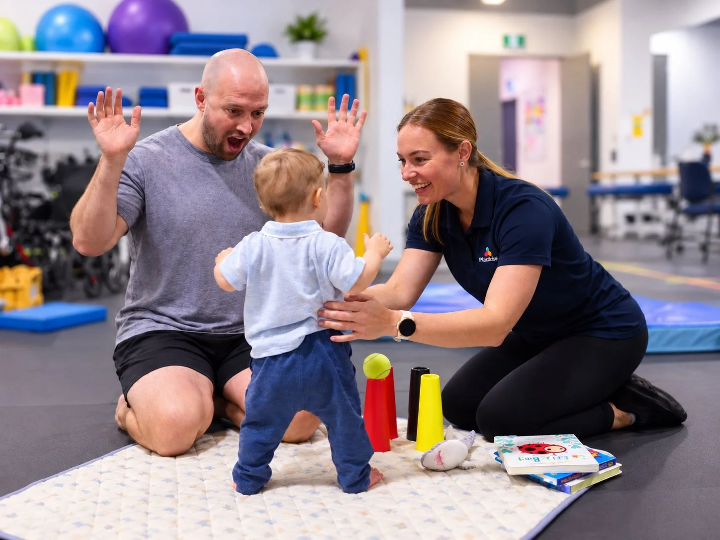 Physiotherapist and parent helping a toddler practise standing