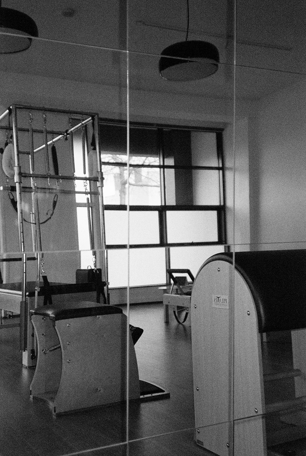 A grayscale photo of a therapy or fitness room with exercise equipment, a mirror, and large windows letting in natural light.