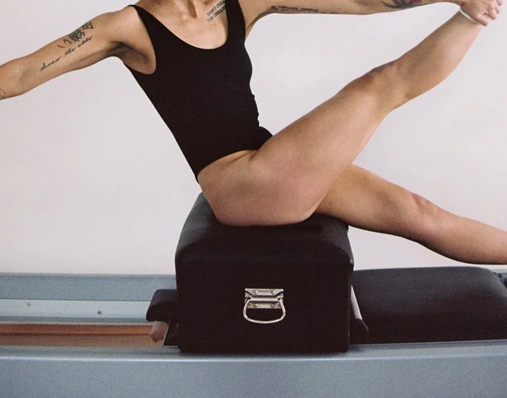 A person performing an acro yoga pose, balancing on their hands and feet, supported by a black prop.