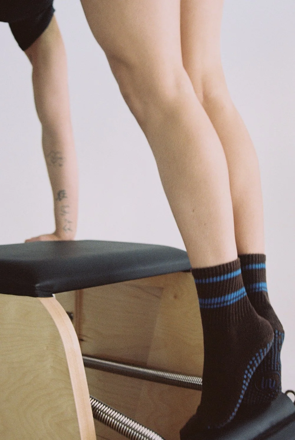 Person doing a Pilates exercise on a reformer machine, wearing black socks with blue stripes.