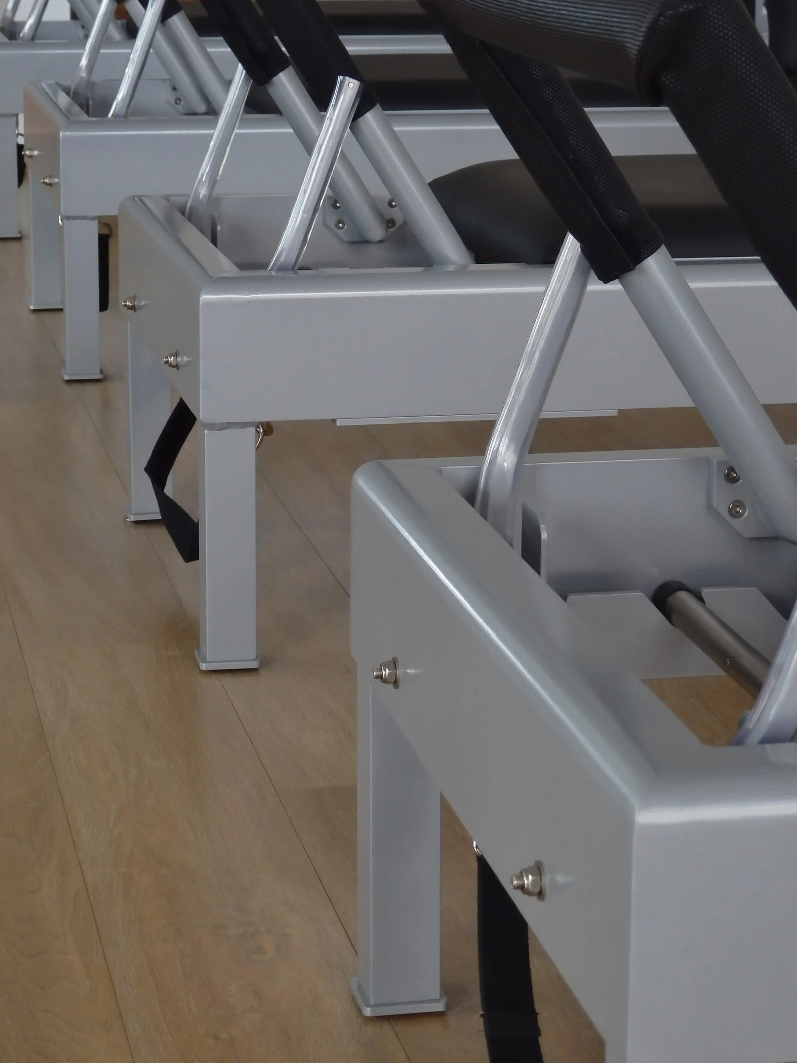 A row of exercise or physical therapy equipment, each with a padded seat and metal frame, on a wooden floor.