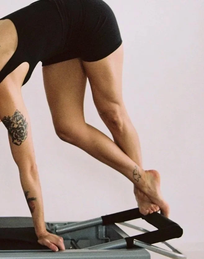 A woman is doing a handstand on a treadmill, with her legs bent and connected to the treadmill's handrails, demonstrating flexibility and strength.