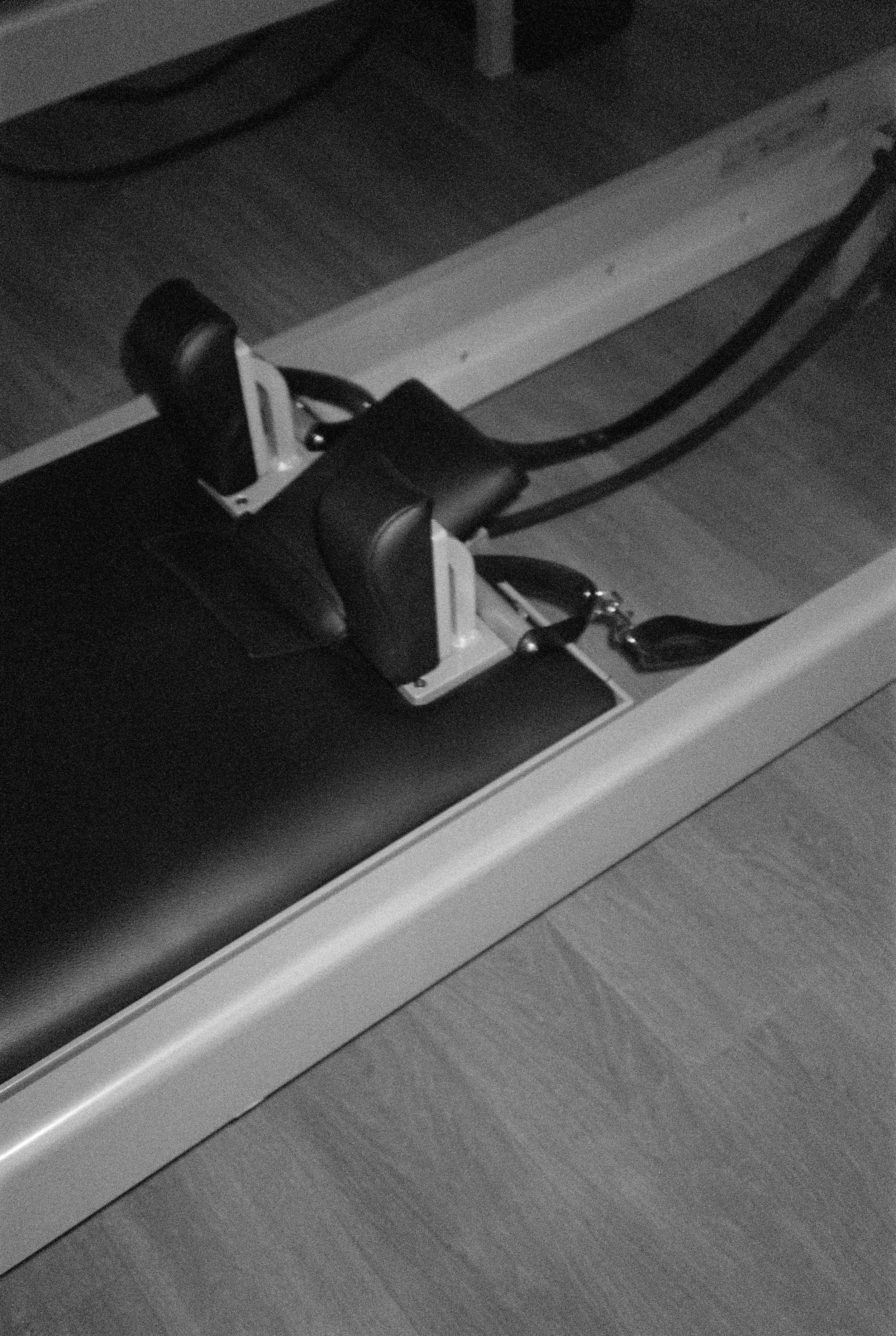 A black and white photograph of a rowing machine placed on a wooden floor.