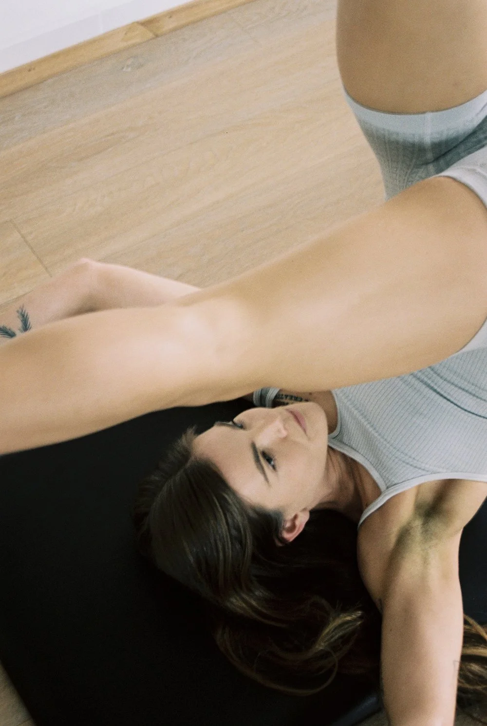 A woman lying on the floor, reaching above her head, with a young man balancing on top of her.