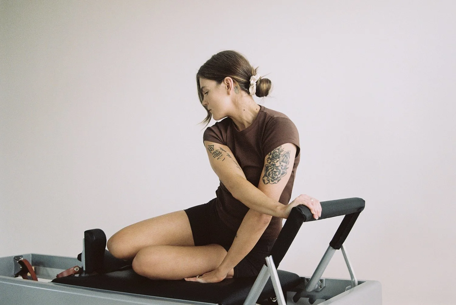 Woman with tattoos sitting on Pilates reformer machine in a neutral space