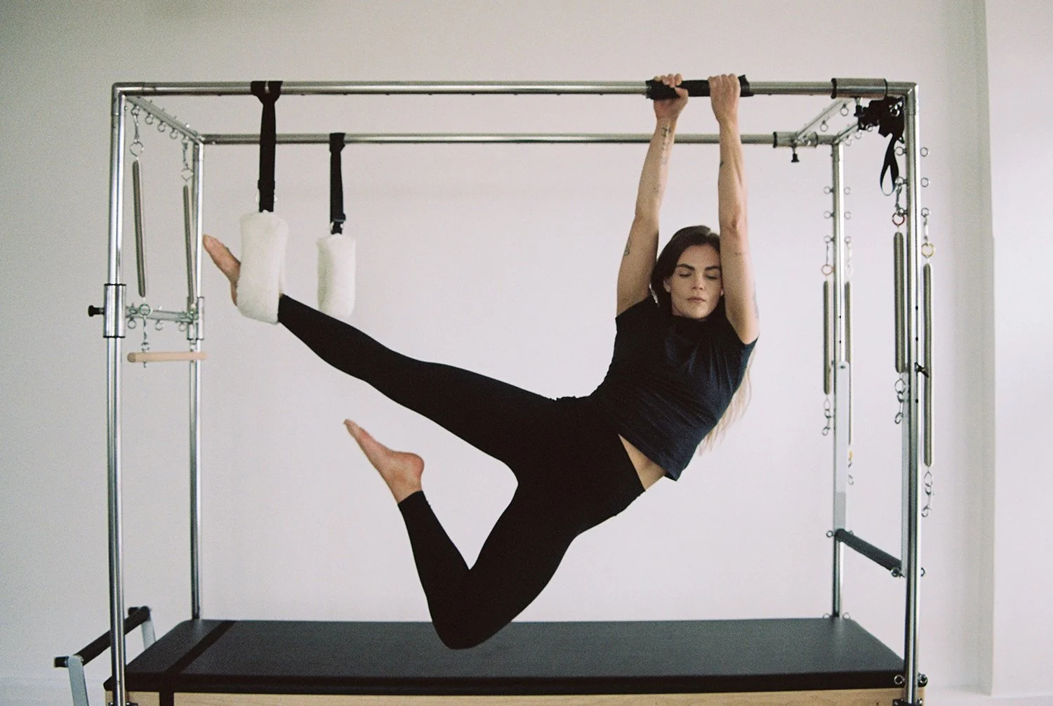 Woman practicing aerial dance or yoga on a metal fitness frame, hanging with one leg hooked on a strap and holding onto the frame with both hands.