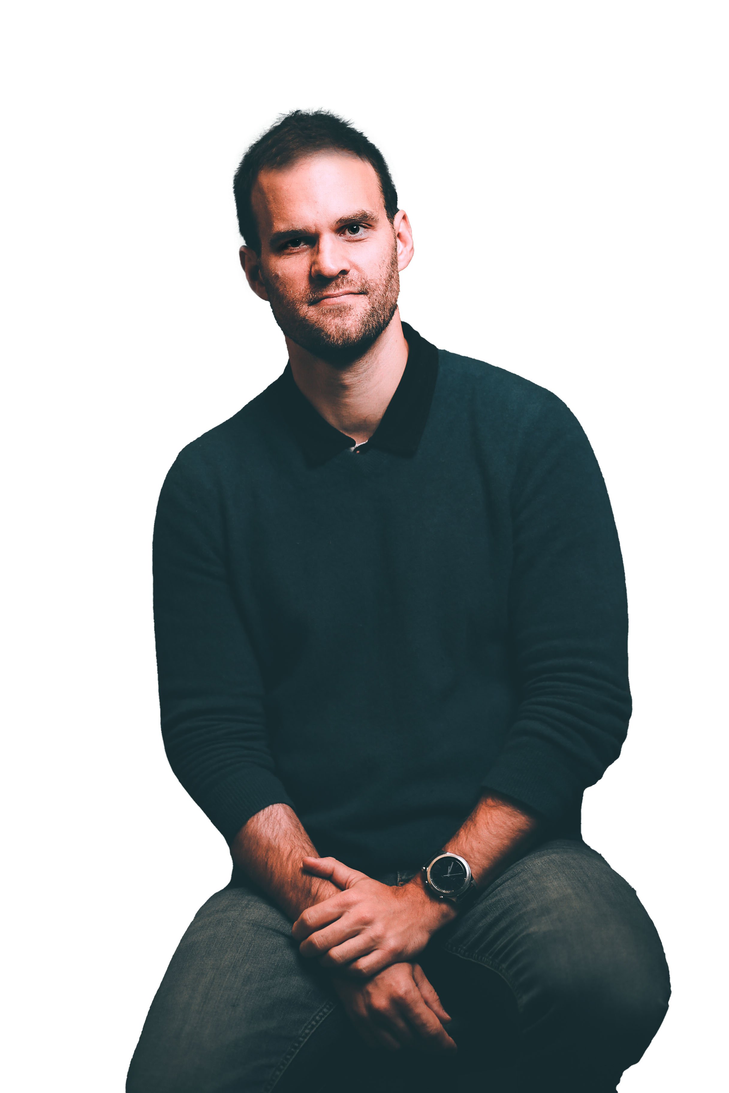 Man seated with thoughtful expression, wearing a dark sweater and jeans, against a plain white background.