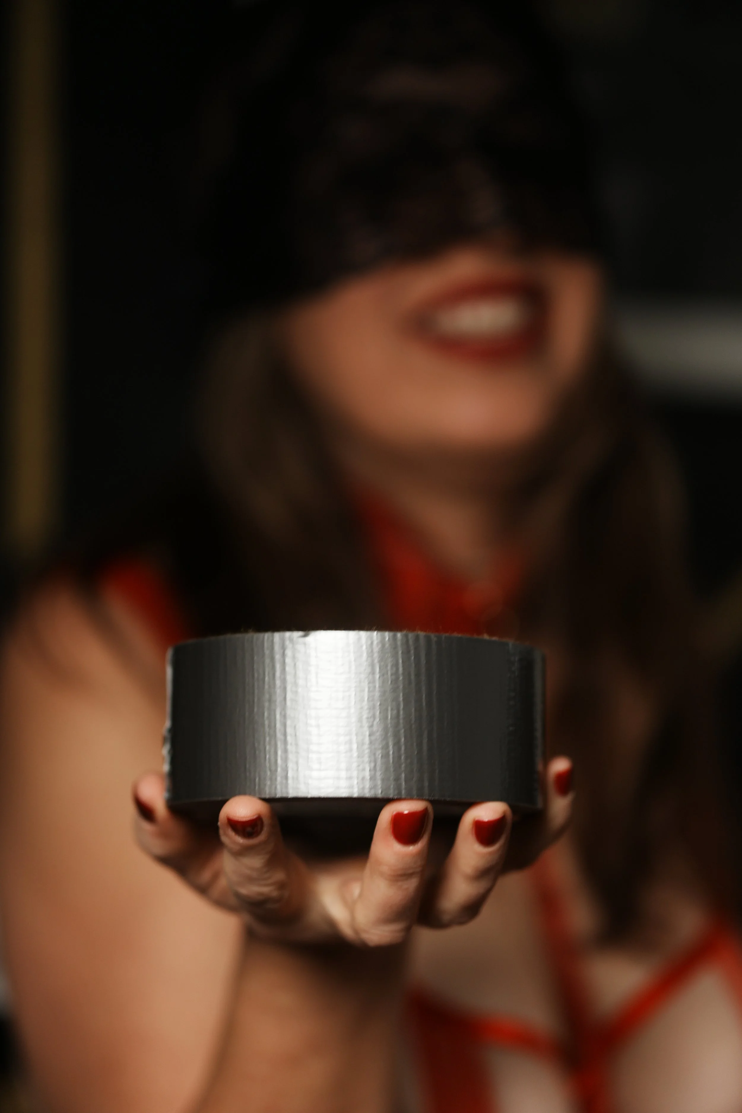 A woman with nails painted red is holding a metallic round object, with a blurry background of her face smiling