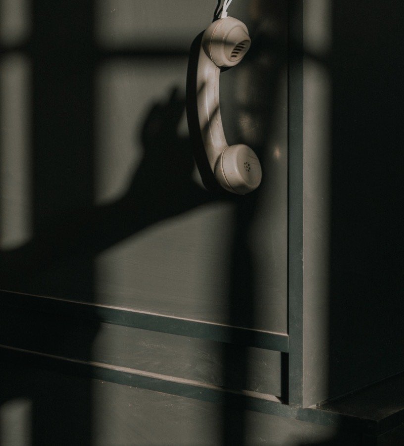 Old beige rotary telephone hanging on a gray wall, casting a shadow.