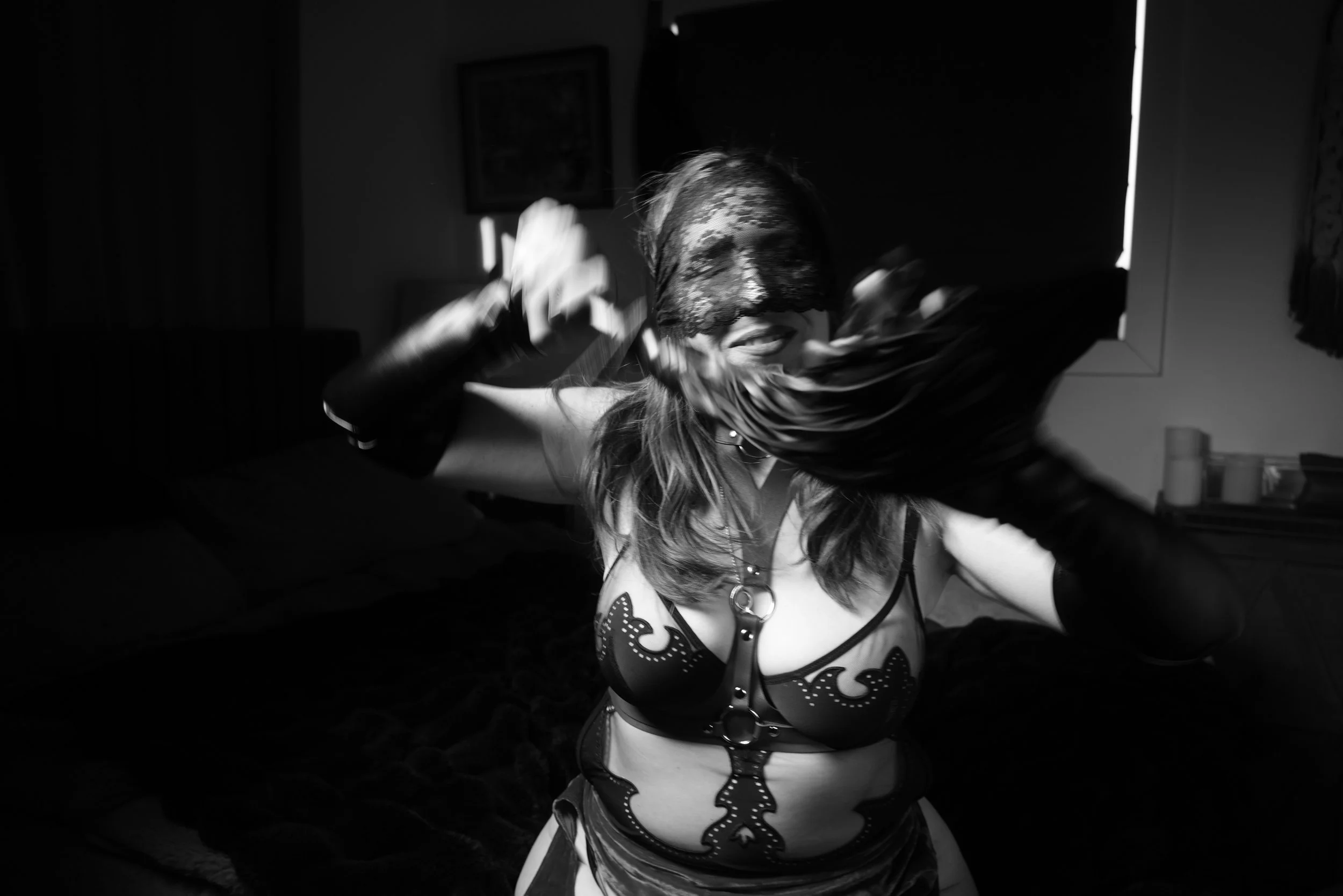 A woman wearing a lacy eye mask and a costume with skull and rose patterns, smiling and dancing in a dimly lit room.