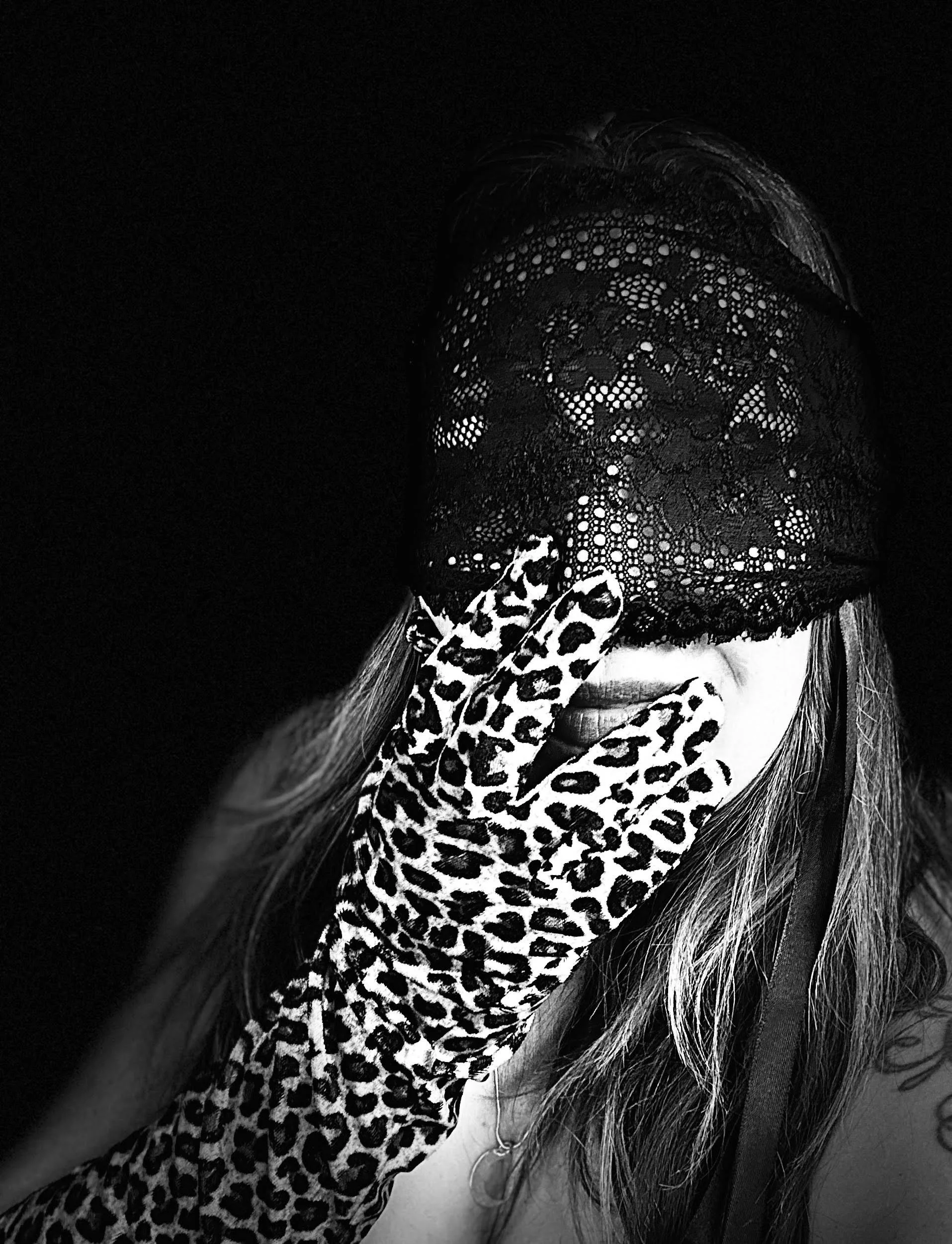 A person wearing lace fabric and leopard print gloves, covering part of their face with long hair visible on the right side.