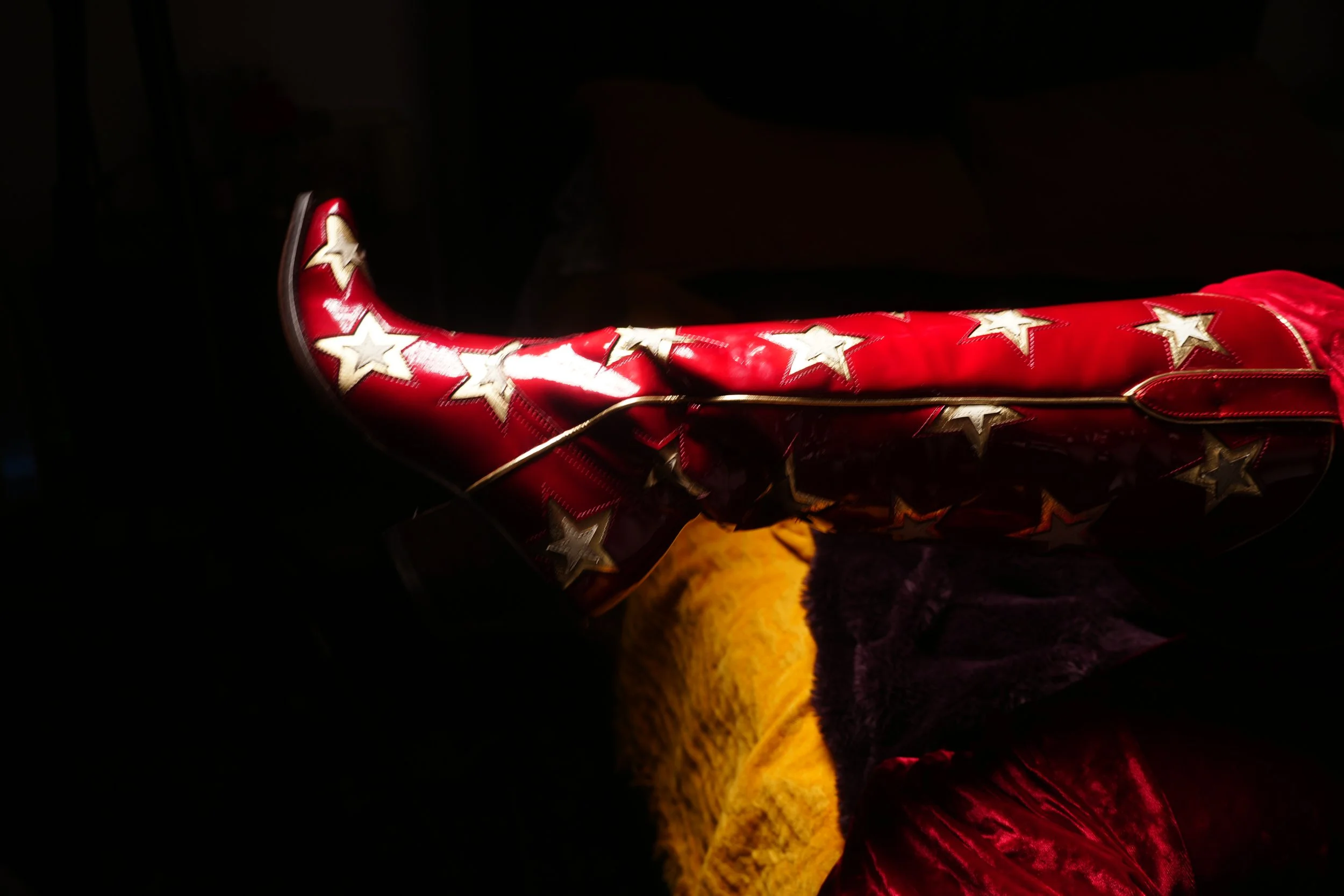 A red cowboy boot with white stars, displayed against a black background.