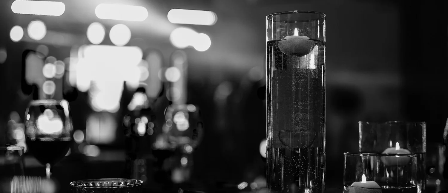 Floating candles in tall glass vessels on an event table, with stage lights blurred behind.
