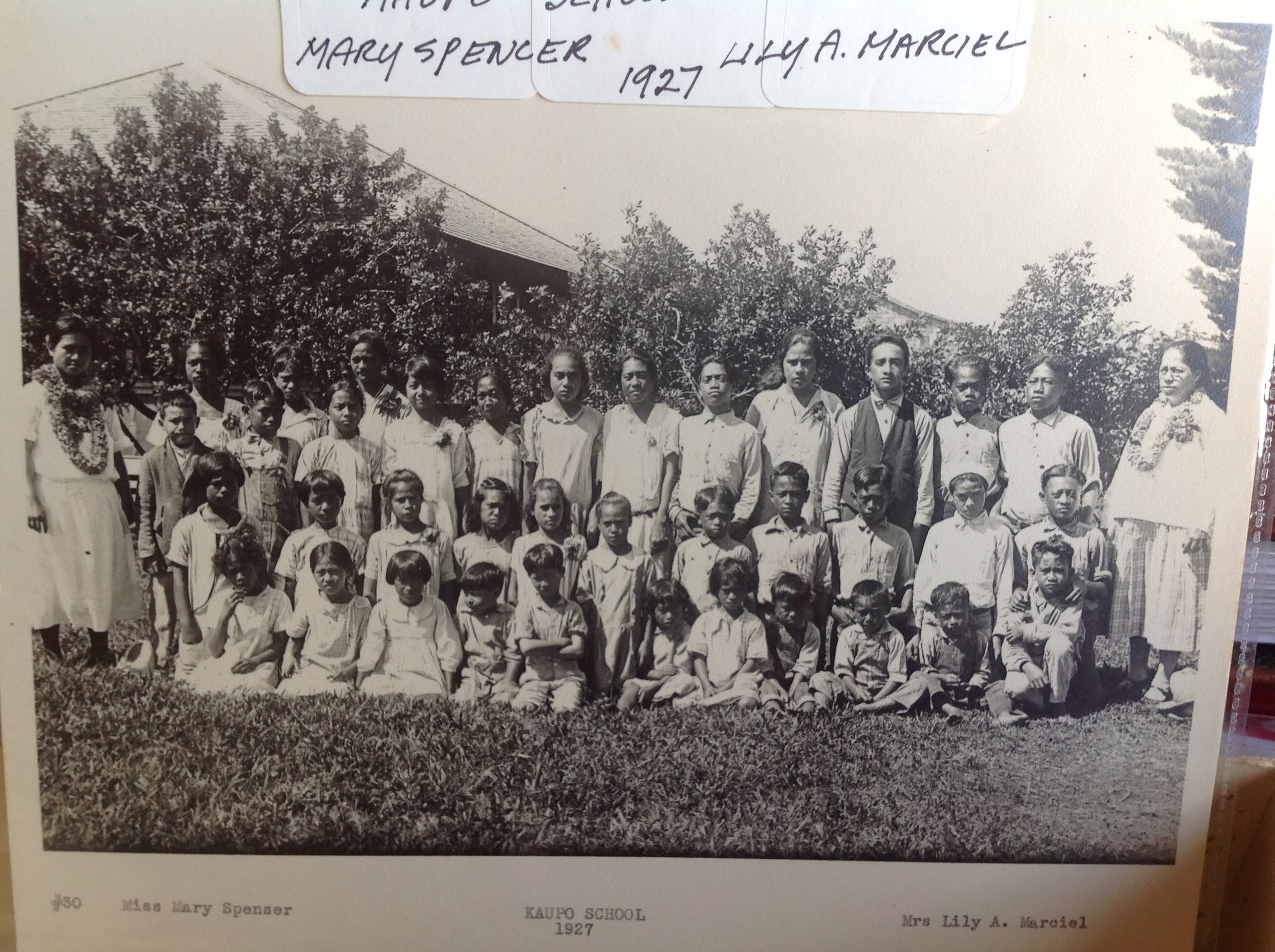 Group photo of students and teachers at Kaupo School in 1927, with children standing and sitting outdoors, surrounded by trees.